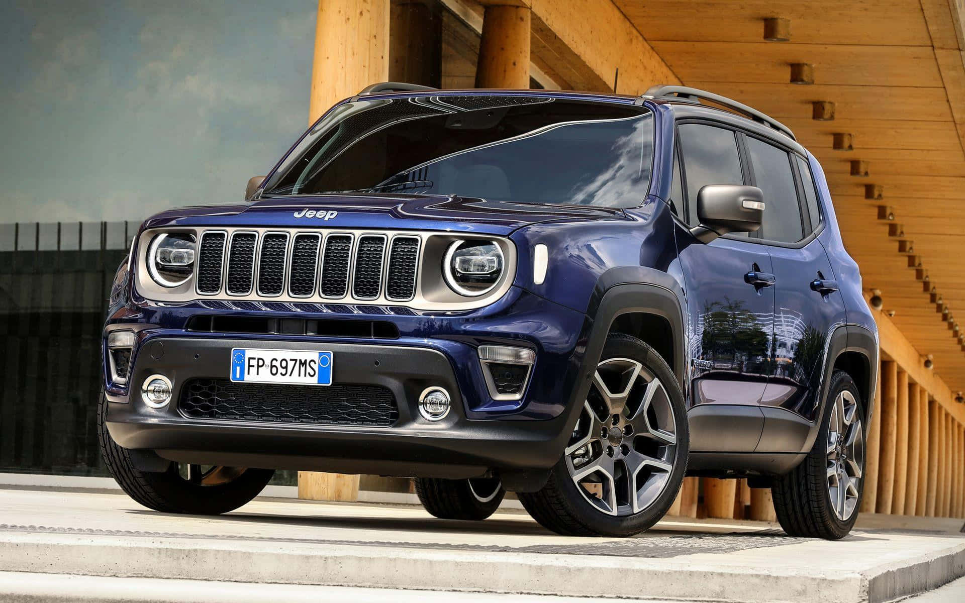 Jeep Renegade 桌布 壁紙 — 一架時尚的藍色Jeep Renegade SUV停放在混凝土平台上，旁邊是木樓梯，天空多雲。