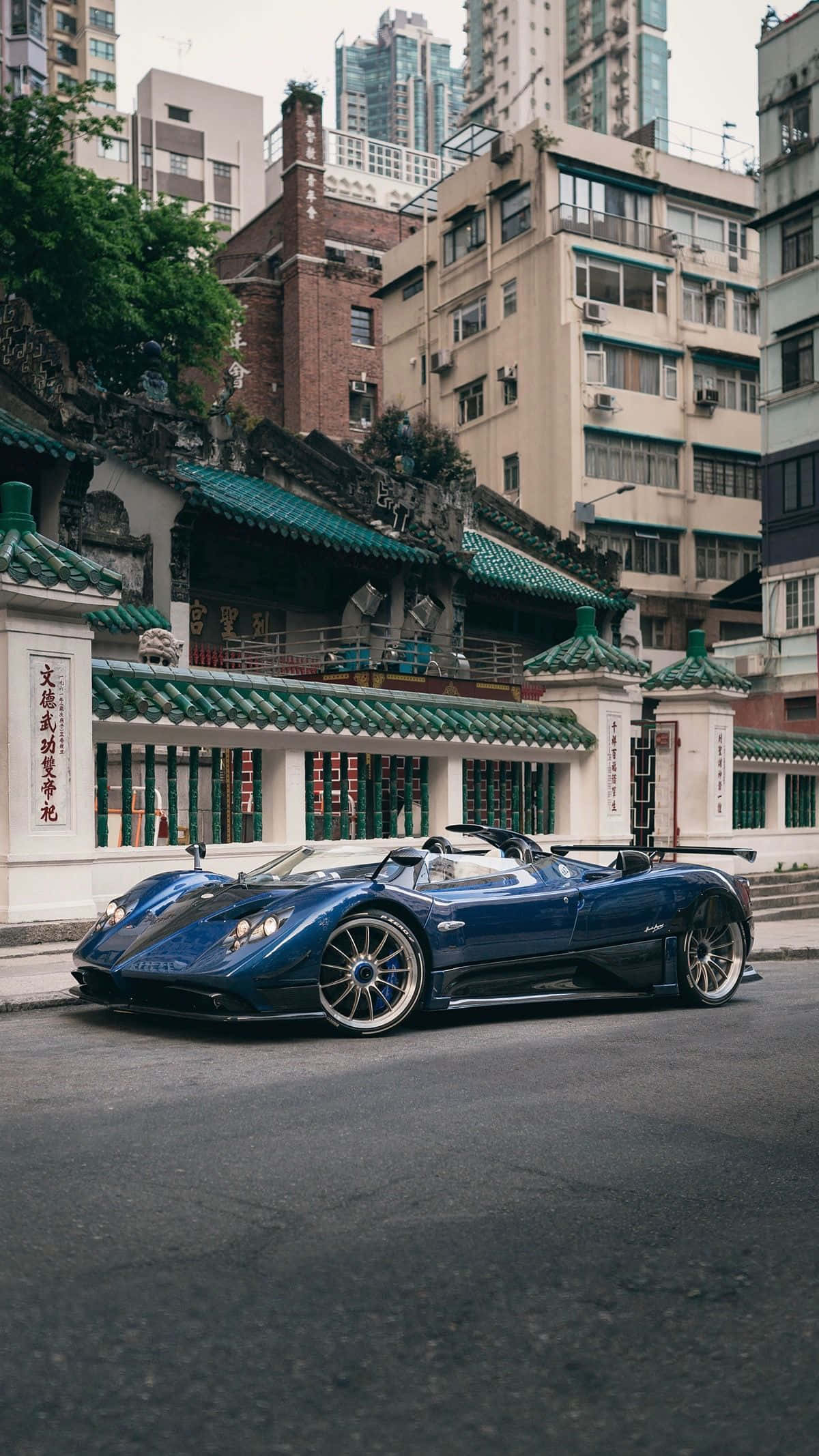 Pagani Zonda Hp Barchetta 桌布 壁紙 — 一輛時尚的藍色跑車停泊在傳統中式寺廟旁邊的街道上，寺廟有綠色瓦頂。