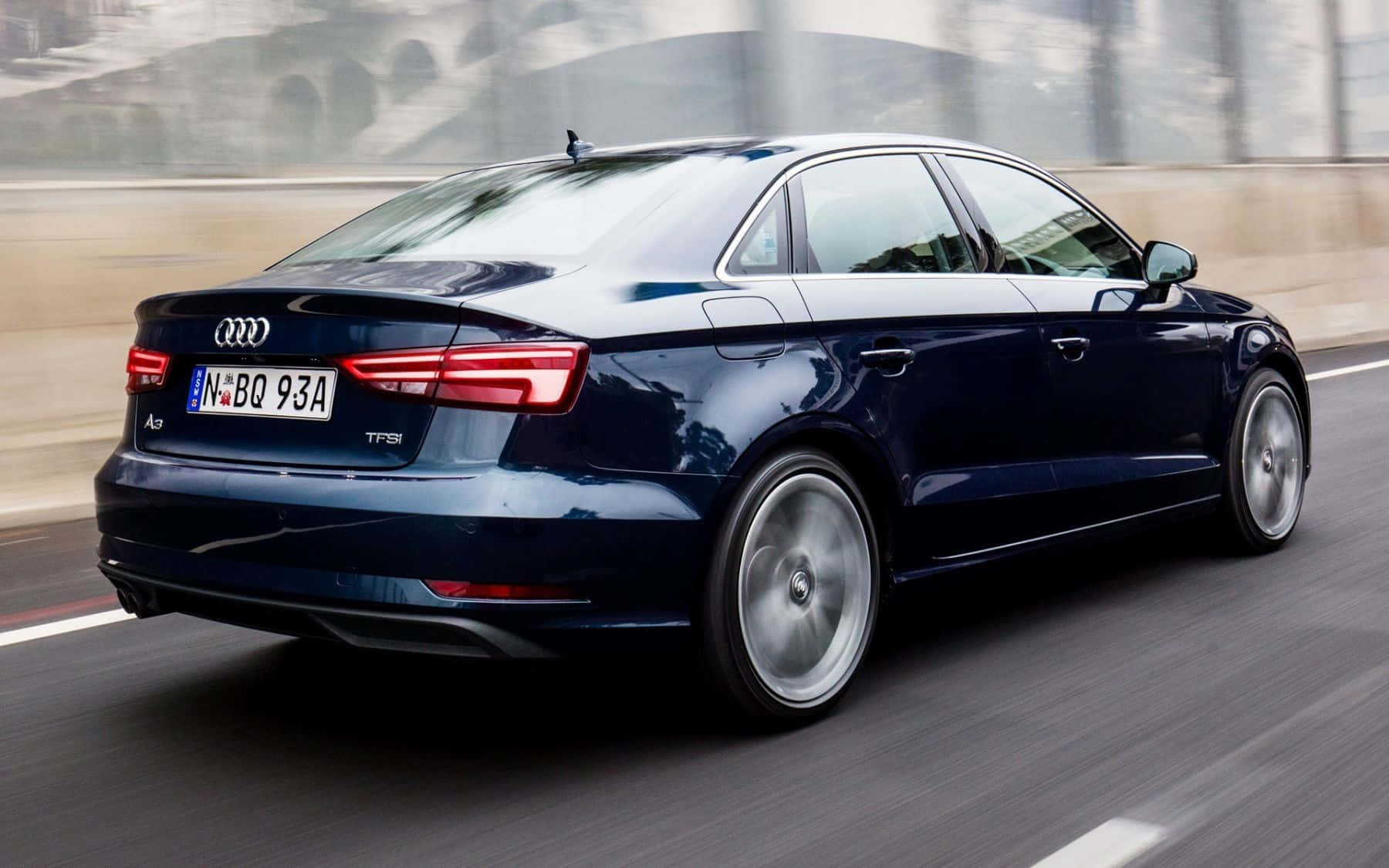 Audi A3 桌布 壁紙 — 一輛時尚的深藍色奧迪A3轎車在模糊的城市道路上疾馳，動態模糊強調了其動態運動。