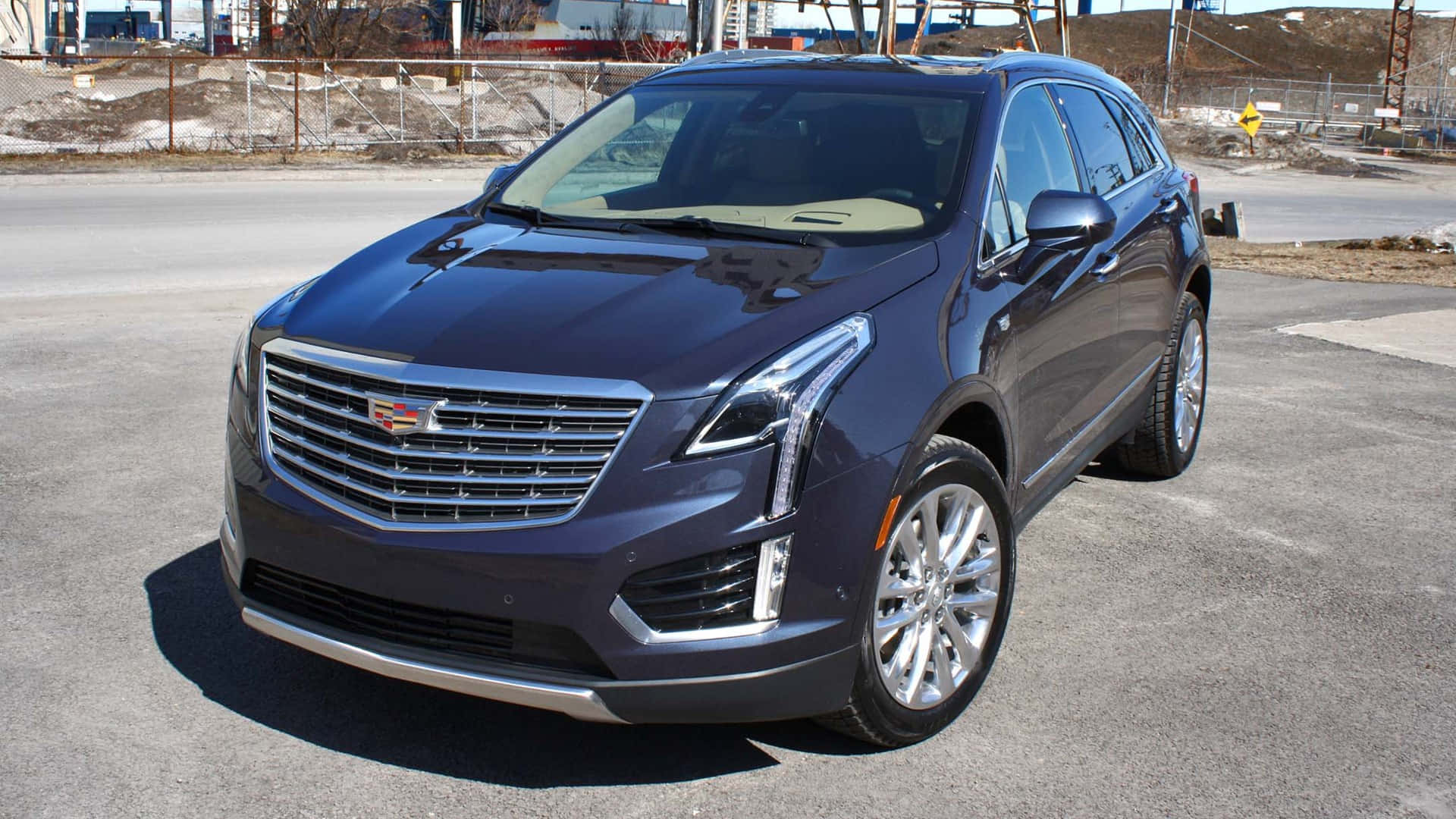 Cadillac Xt5 桌布 壁紙 — 一輛時尚的深藍色Cadillac XT5 SUV停在柏油路上，背景是建築工地，在明亮的日光下。