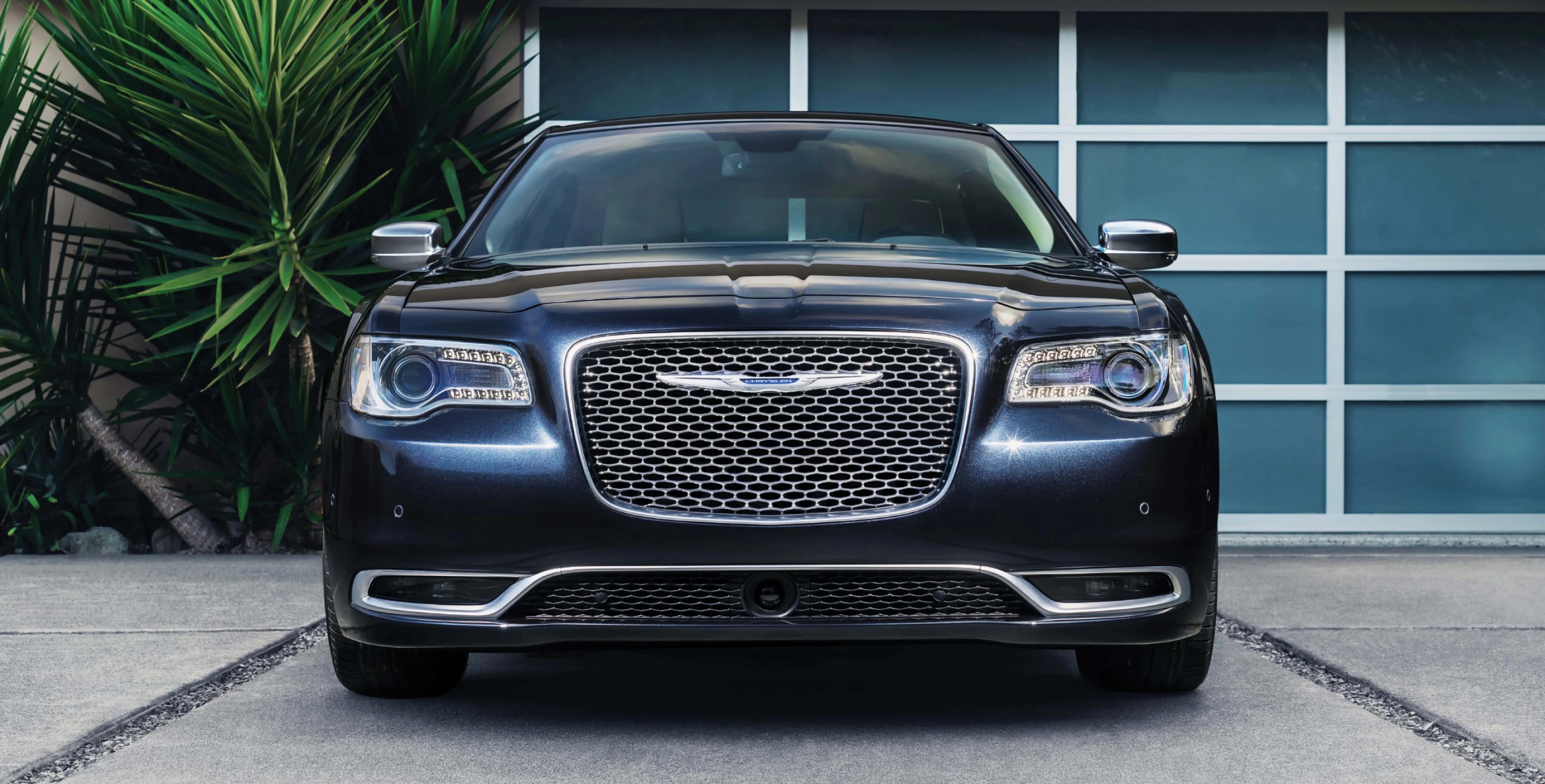 Chrysler 300 桌布 壁紙 — 一輛時尚深藍色克萊斯勒300轎車面向現代藍色車庫門，旁邊有茂密的綠色棕櫚樹。