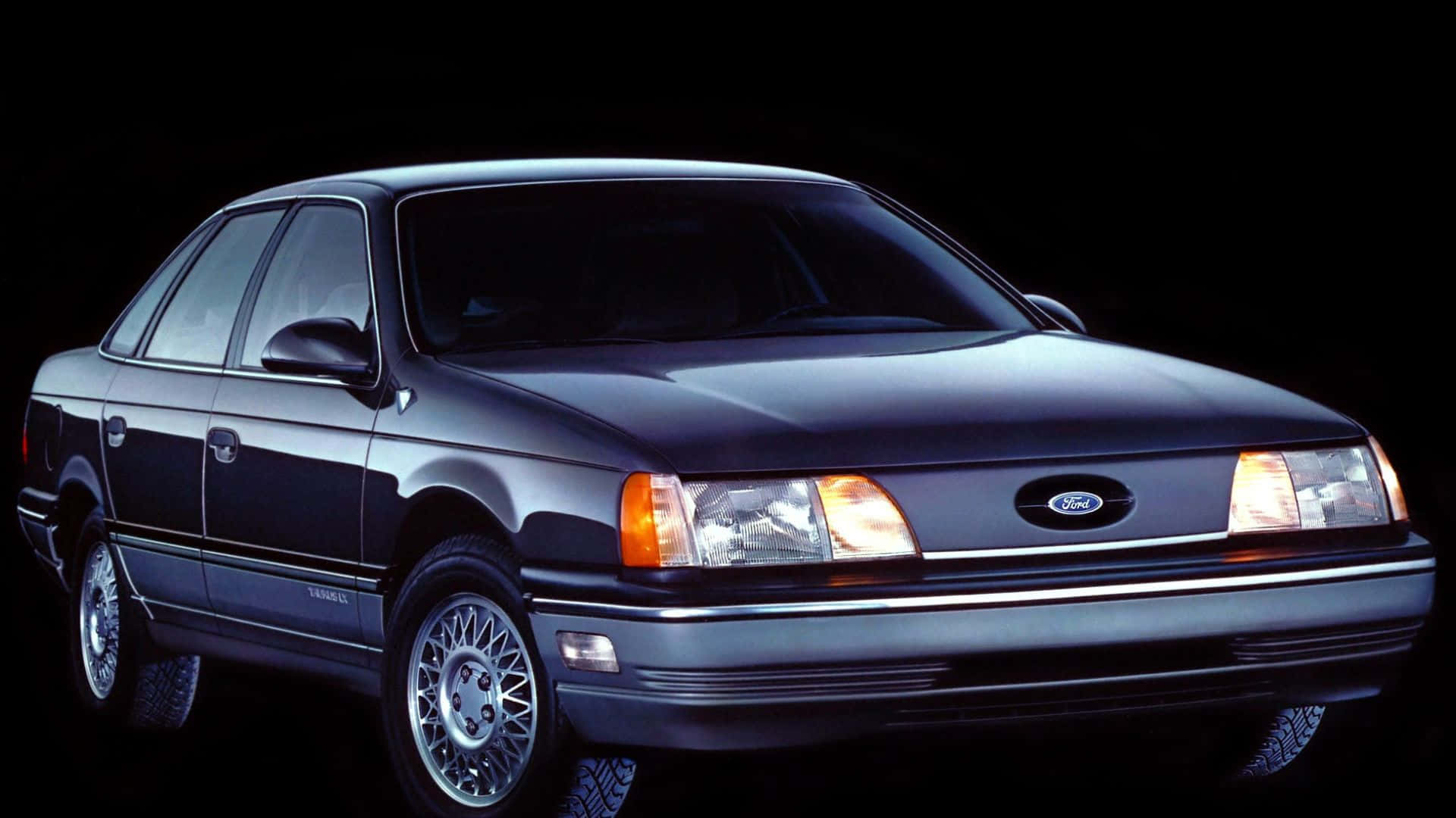 Ford Taurus 桌布 壁紙 — 一輛時尚的深藍色福特 Taurus 轎車在黑色背景下的攝影棚燈光中閃耀，車頭燈亮起。
