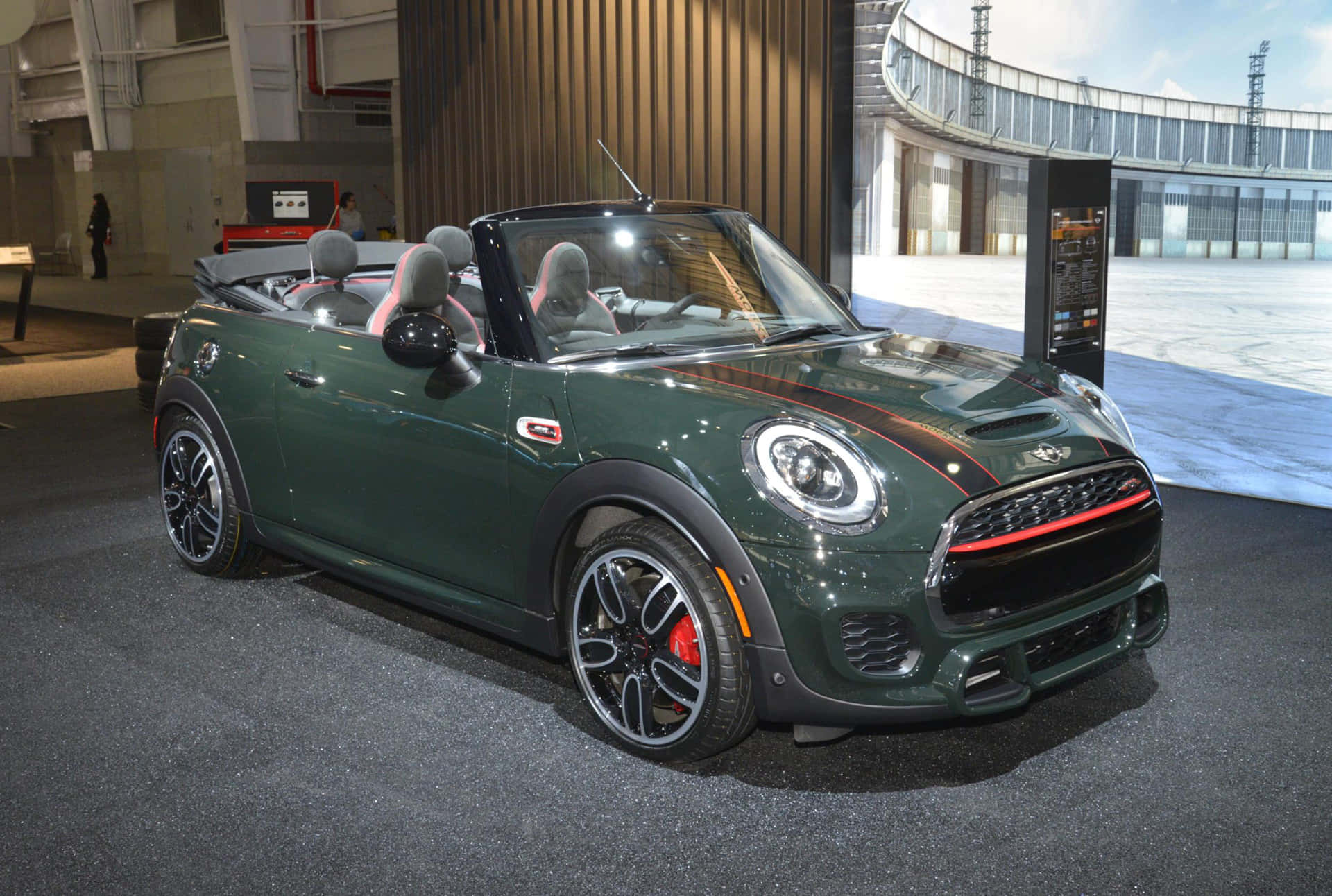 Mini Cooper Convertible 桌布 壁紙 — 一輛時尚的深綠色MINI敞篷車，帶有紅色點綴和黑色輪圈，在室內明亮燈光下展示。