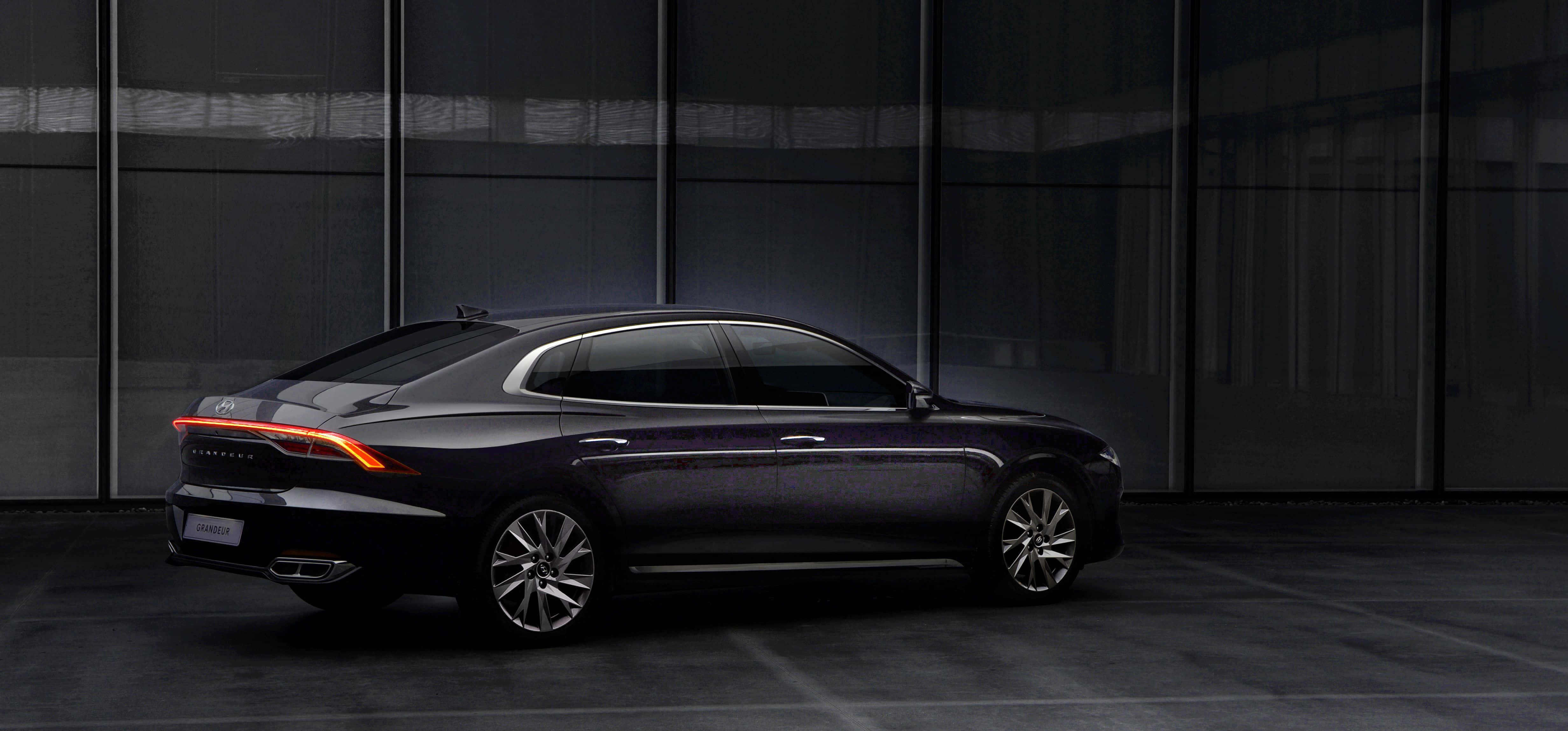 Hyundai Azera 桌布 壁紙 — 一輛時尚深色轎車帶有發光尾燈，在簡約都市環境中停靠於現代玻璃牆前。
