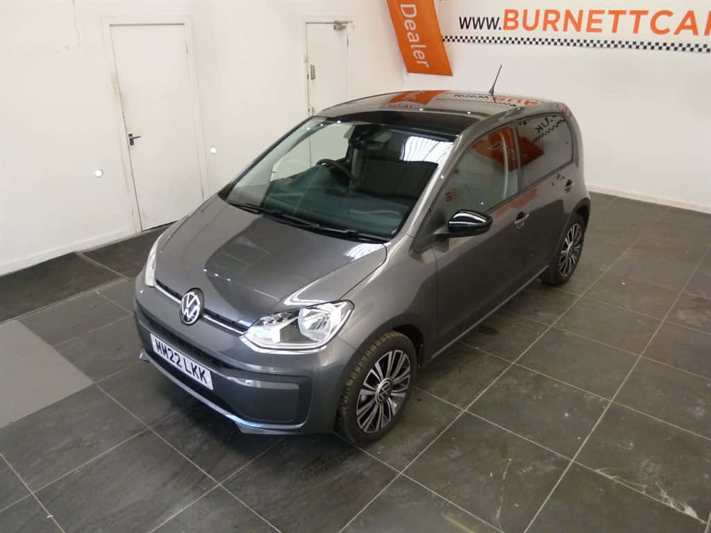  壁紙 — 一輛時尚的灰色Volkswagen up! 停放在室內瓷磚地板上，在明亮的展廳燈光下。