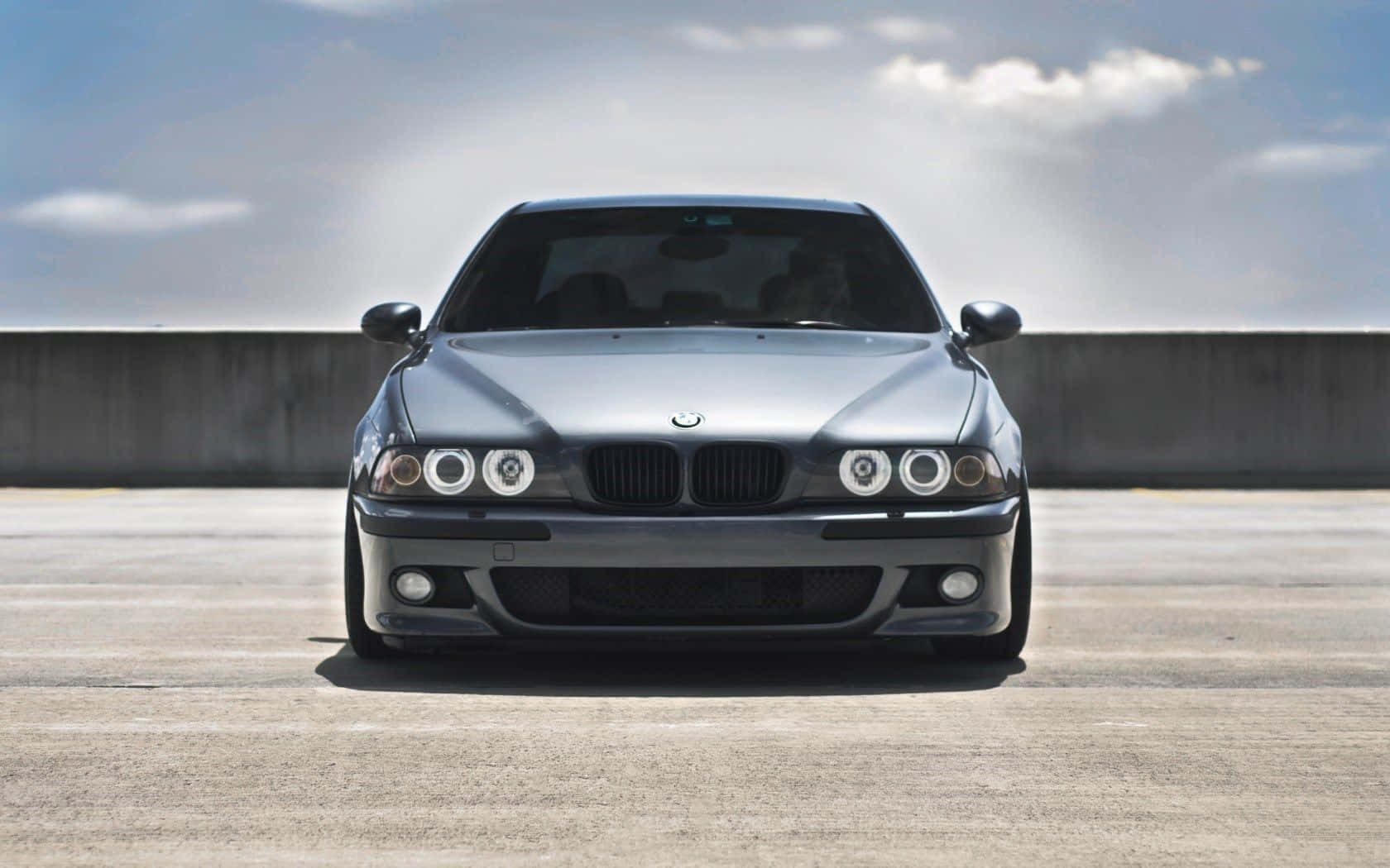 Bmw M5 桌布 壁紙 — 一部時尚的銀色BMW E39轎車在部分多雲的天空下，正面朝前停在混凝土表面上。