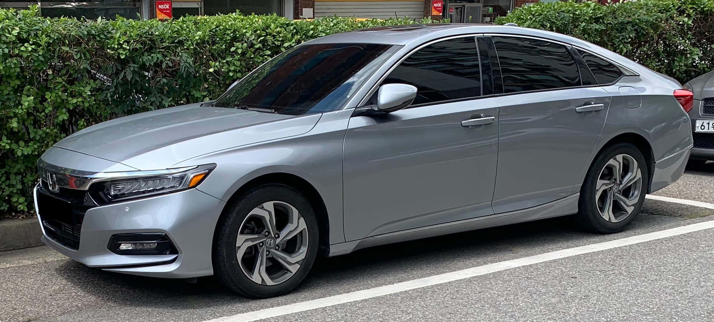 Honda Accord 桌布 壁紙 — 一輛時尚的銀色本田轎車停在綠色籬笆旁的停車場，在明亮的日光下。