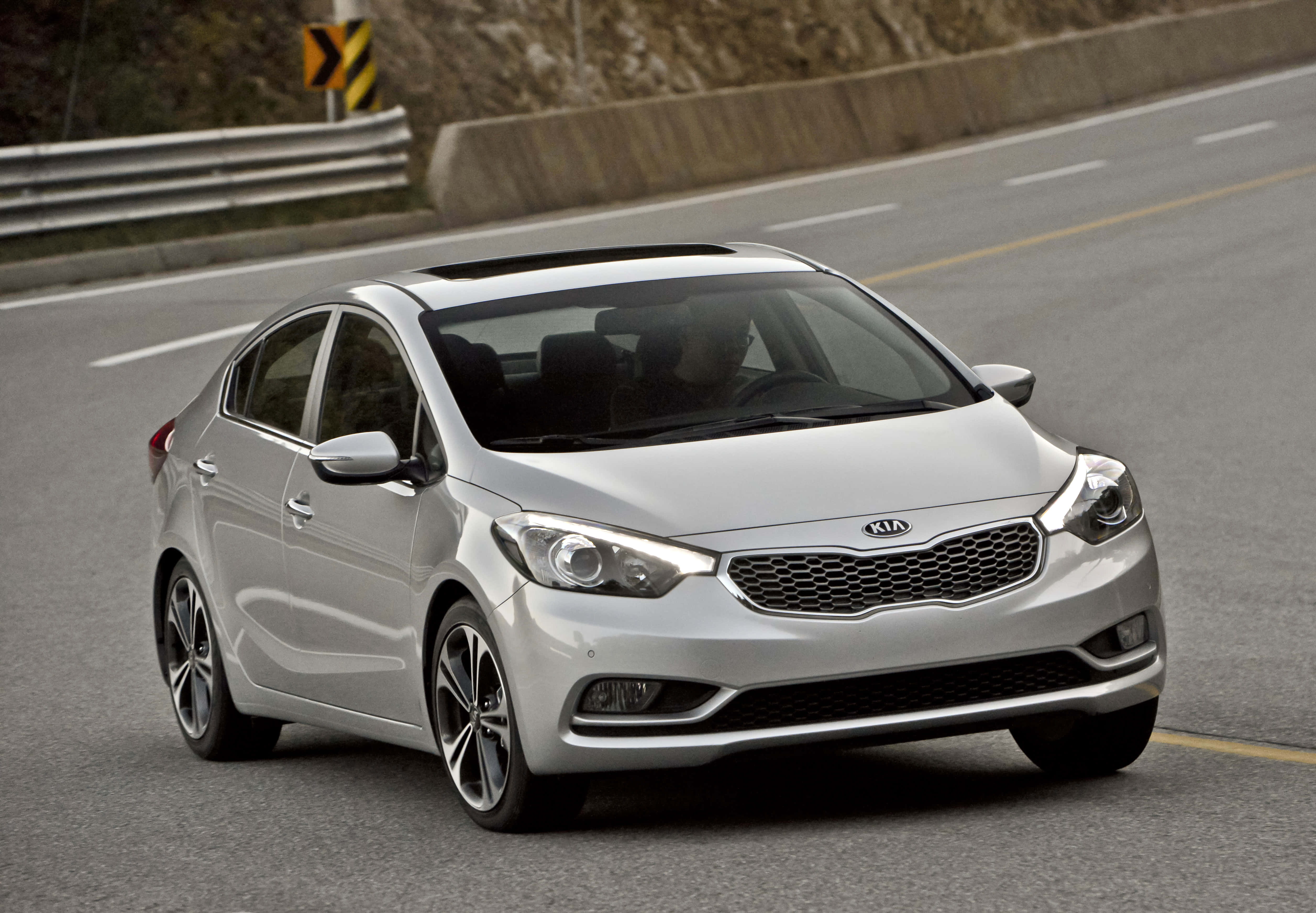 Kia Forte 桌布 壁紙 — 一輛時尚的銀色Kia轎車沿著蜿蜒的山路行駛，背景有護欄和岩石地形。