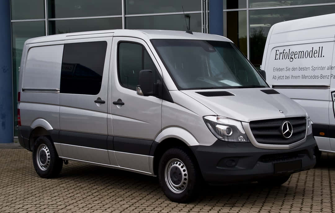 Mercedes Benz Sprinter 桌布 壁紙 — 一輛時尚的銀色 Mercedes-Benz Sprinter 客貨車停放在現代玻璃建築前的鋪砌停車場上。