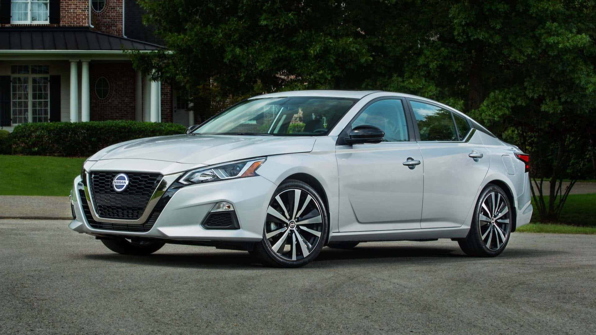 Nissan Altima 桌布 壁紙 — 一輛時尚的銀色日產Altima轎車停在磚房前的車道上，周圍有茂密的綠樹。