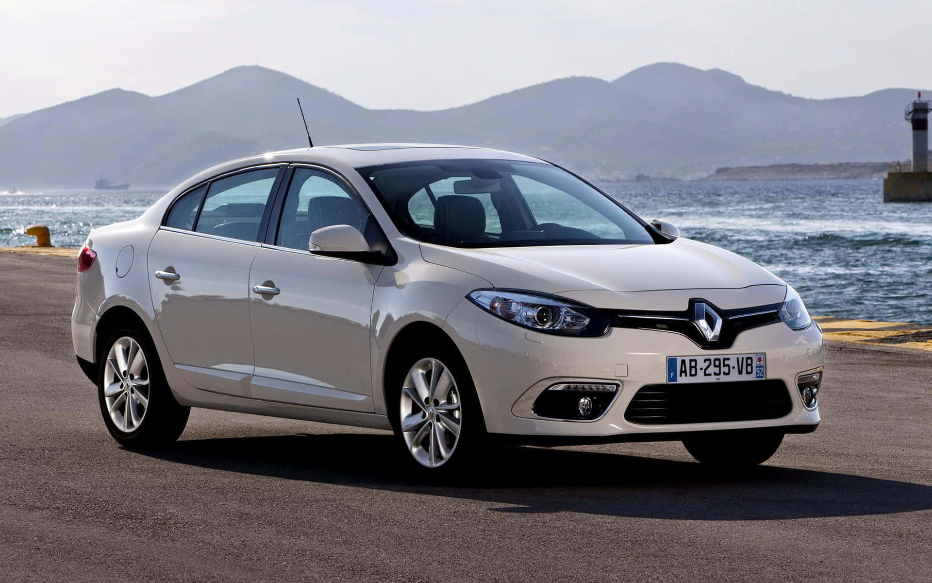 Renault Fluence 桌布 壁紙 — 一輛時尚的銀色雷諾轎車停泊在沿海公路上，背景是山脈和海洋。