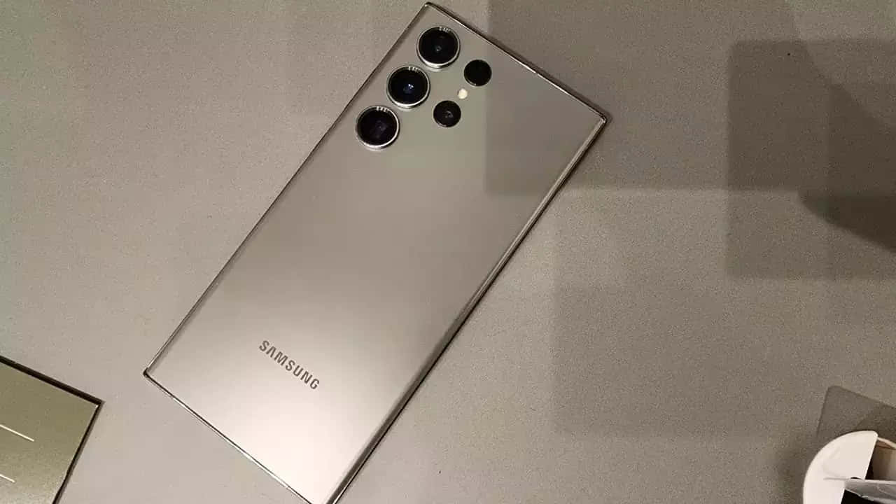  壁紙 — 一部時尚的銀色Samsung智慧型手機，配備四鏡頭陣列，對角放置在簡約的灰色表面上。