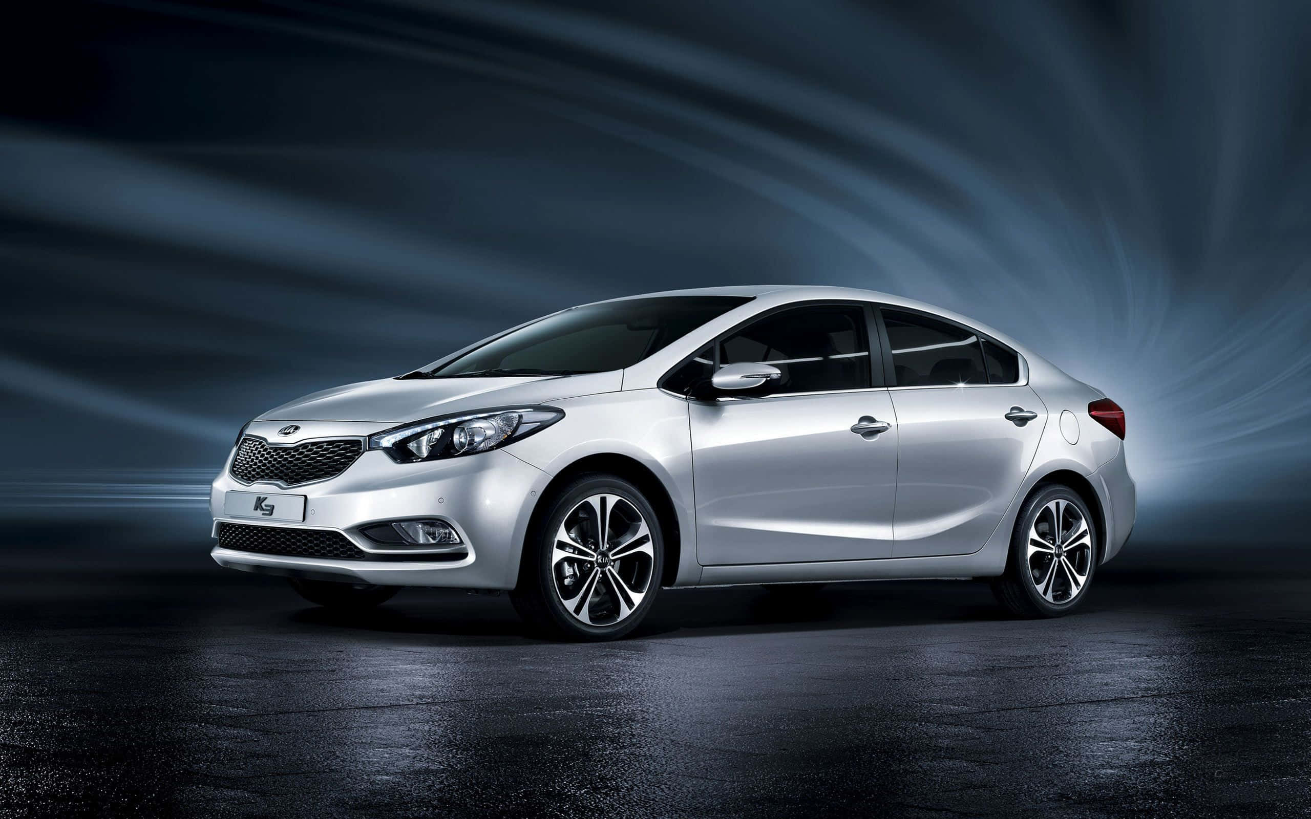 Kia Forte 桌布 壁紙 — 一輛時尚的銀色轎車在黑暗的攝影棚中滑行，身後散發出戲劇性的藍色光條。