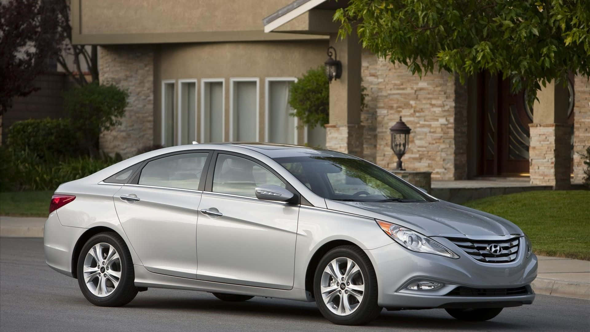 Hyundai Sonata 桌布 壁紙 — 一輛時尚的銀色轎車停放在寧靜的住宅街道上，前面是帶有綠化的石面房屋。