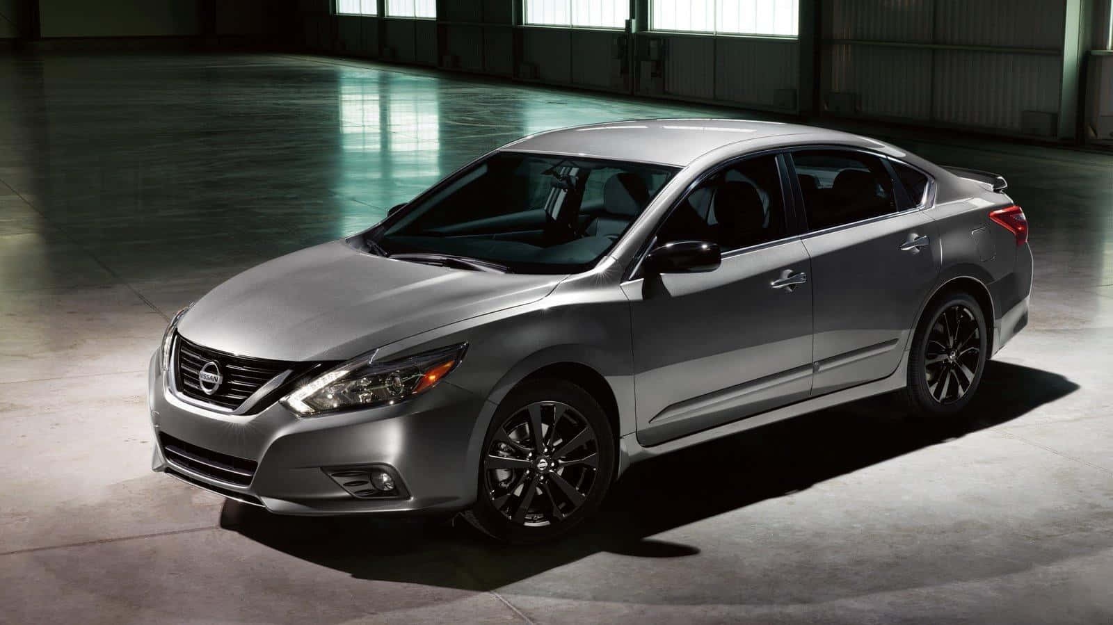 Nissan Altima 桌布 壁紙 — 一輛時尚的銀色轎車搭配黑色輪圈，在寬敞的工業倉庫中於戲劇性燈光下展示。