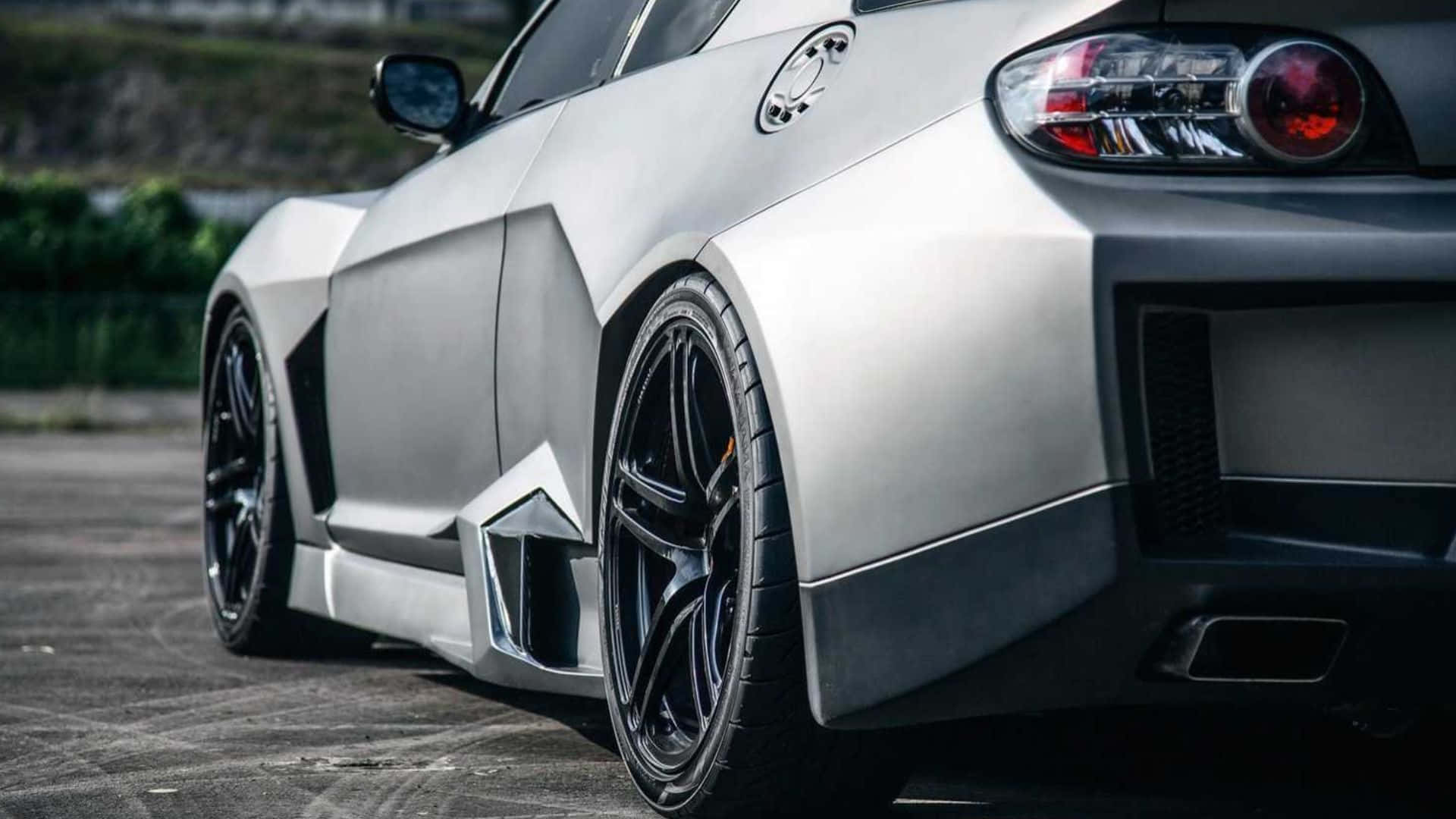 Mazda Rx-8 桌布 壁紙 — 一輛時尚的銀色跑車，配備黑色輪圈和紅色尾燈，停放在鋪砌路面上。