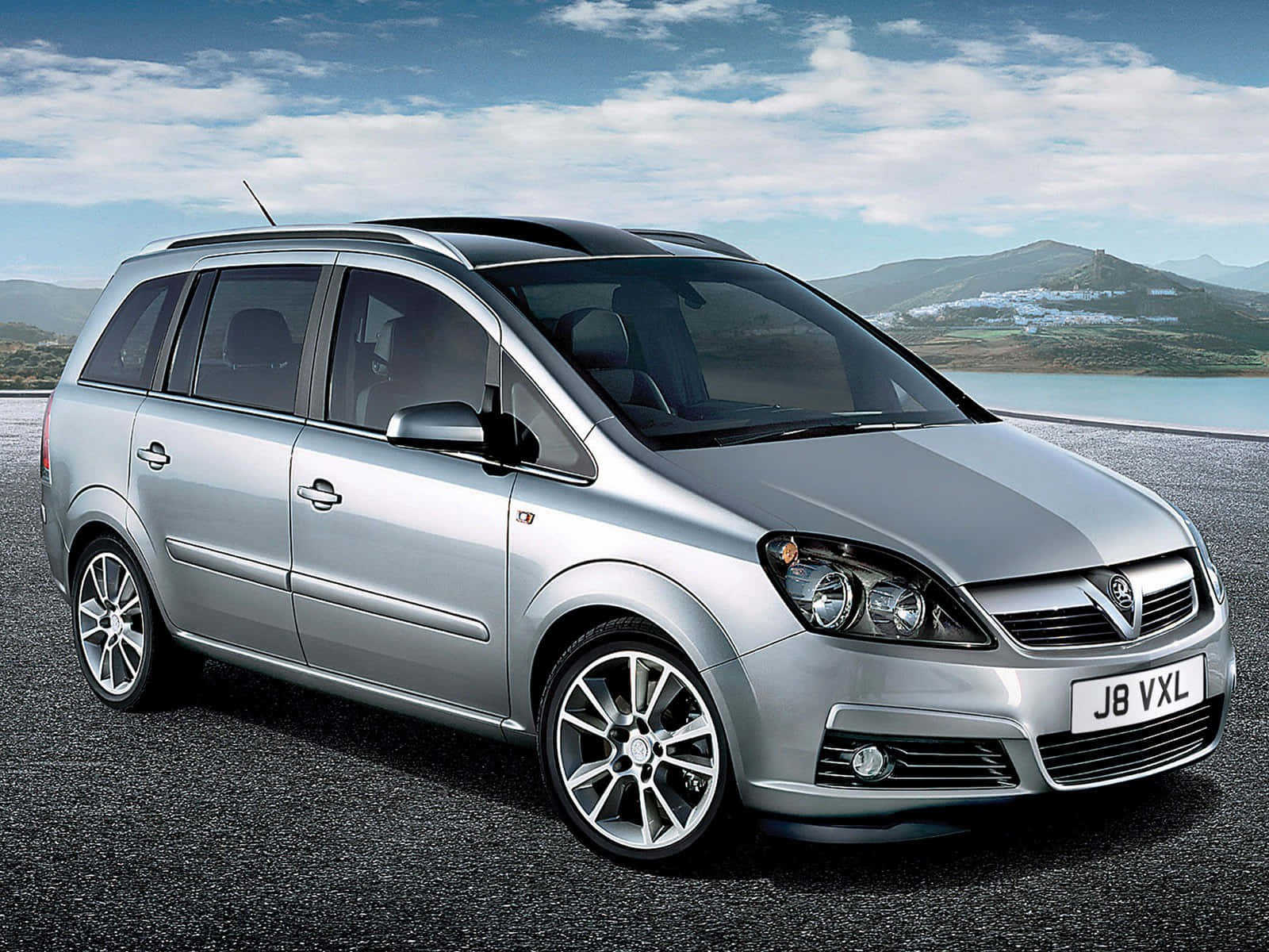 Opel Zafira 桌布 壁紙 — 一輛時尚的銀色Vauxhall Zafira停在柏油路上，背景是山脈和湖泊，天空部分多雲。