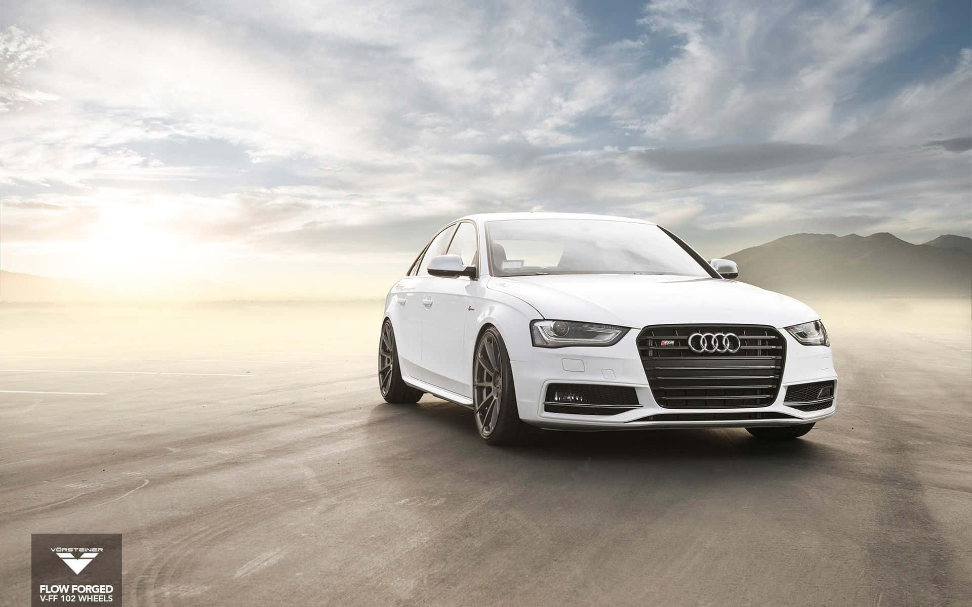 Audi S4 桌布 壁紙 — 一輛配備定制輪圈的時尚白色奧迪轎車，在廣闊的沙漠公路上，背景是戲劇性的多雲天空和遠山。