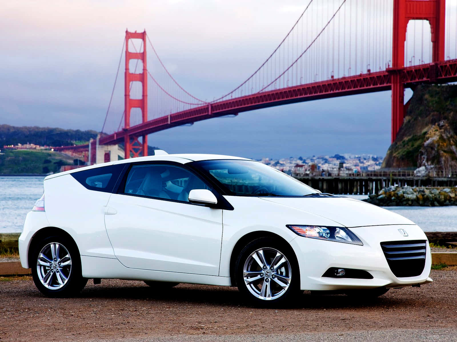 Honda Cr-z 桌布 壁紙 — 一輛時尚的白色跑車停在水邊，背景是標誌性的紅色金門大橋在陰雲密布的天空下聳立。