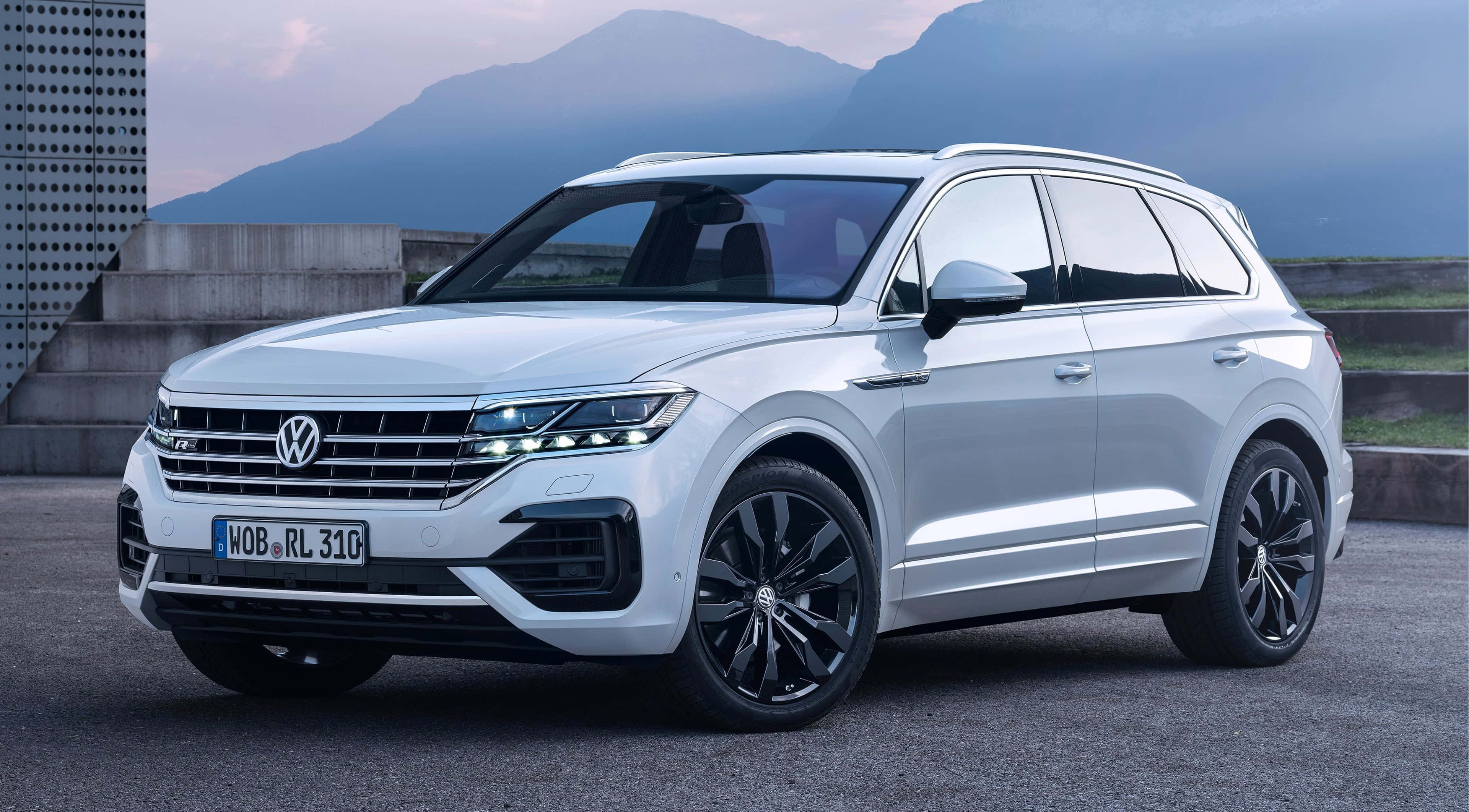 Volkswagen Touareg 桌布 壁紙 — 一輛時尚的白色福斯 Touareg SUV 停放在混凝土平台上，背景是山脈，在柔和的暮色天空下。