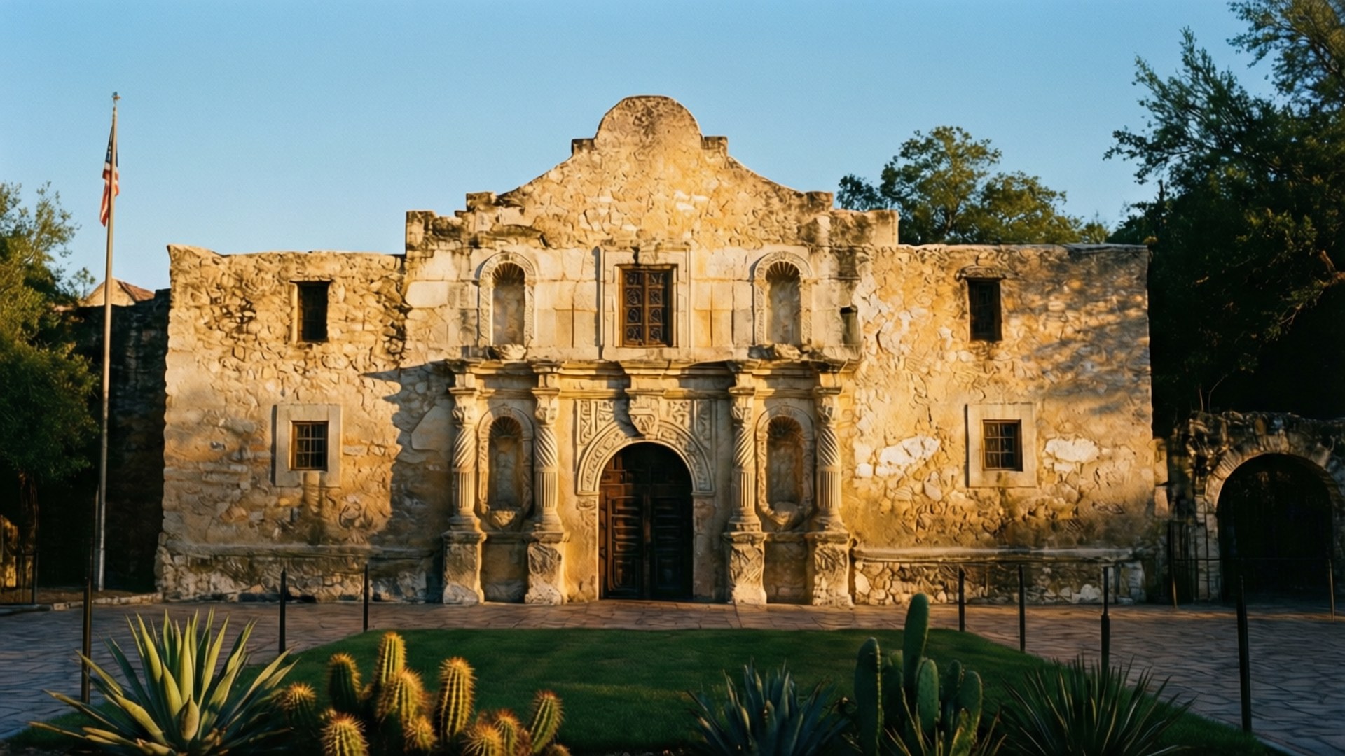 The Alamo at Golden Hour 壁紙 — 陽光灑落在歷史悠久的石造阿拉莫傳教所，前景有仙人掌和綠植，天空清澈湛藍。