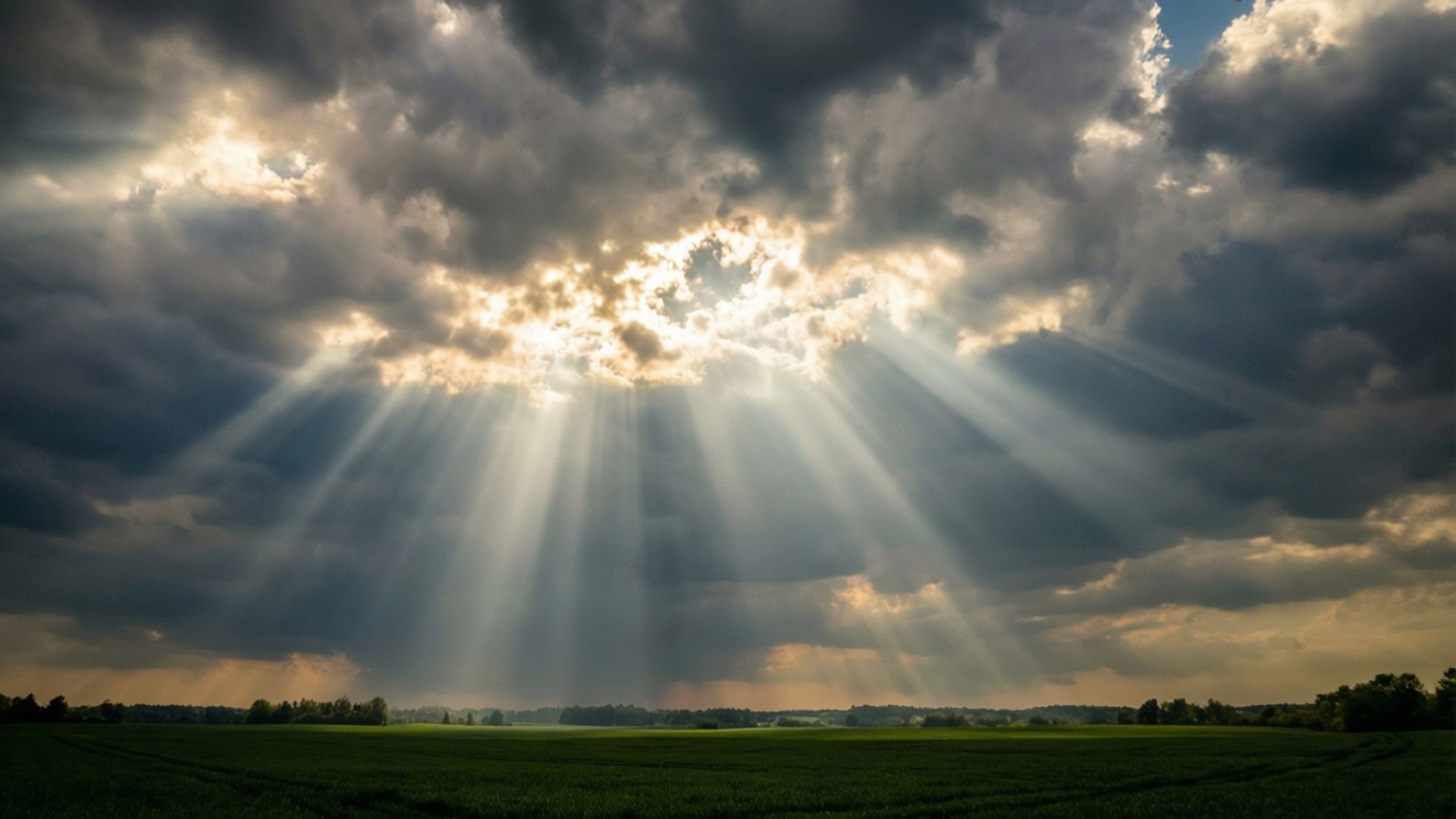 God Rays Over Field 壁紙 — 夕陽穿過黑暗的暴風雲，照耀在廣闊的綠色田野上。