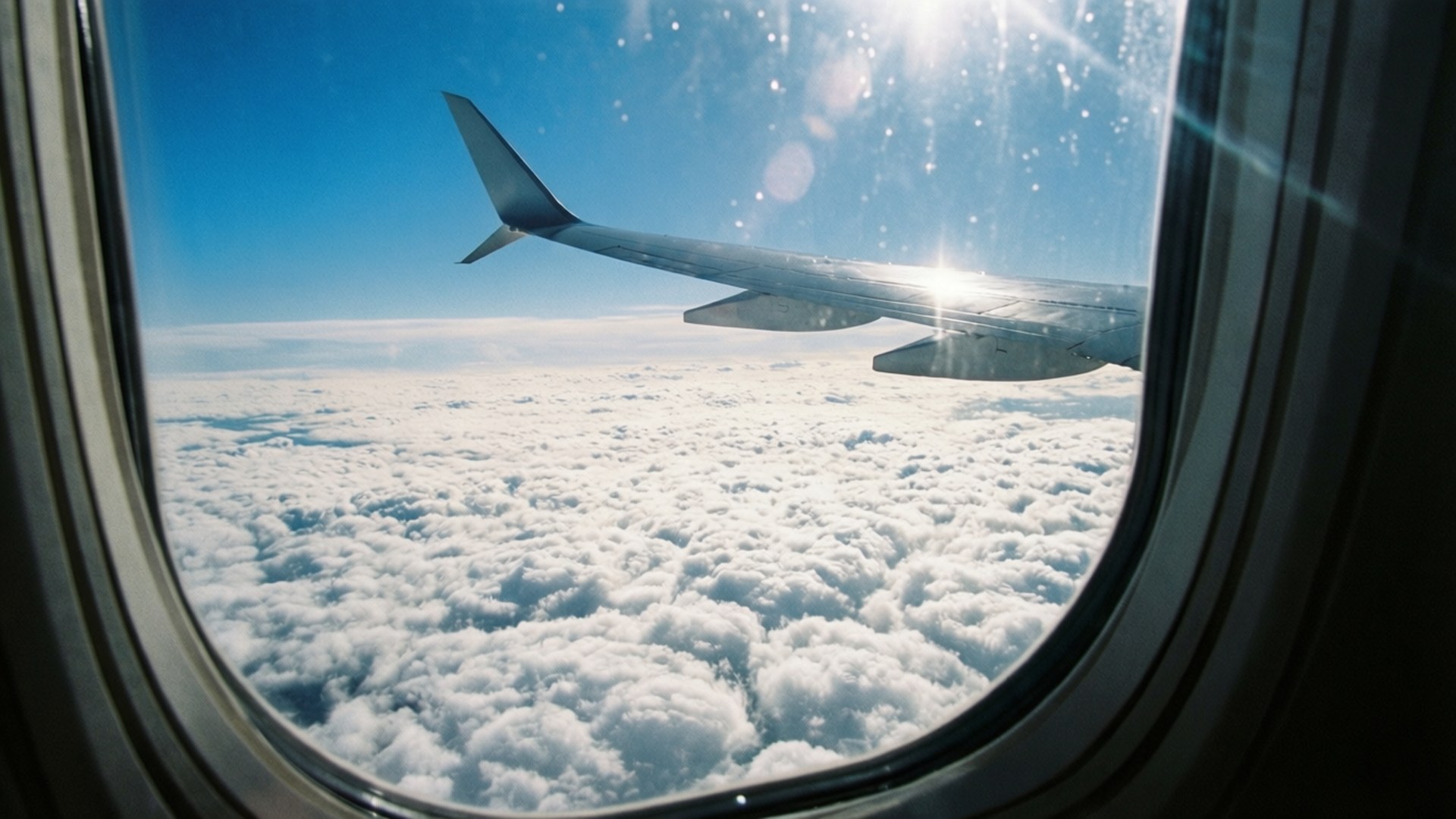 Airplane Window Clouds 壁紙 — 陽光在飛機機翼上閃爍，它在晴朗的藍天下翱翔於無盡的蓬鬆白雲之上。