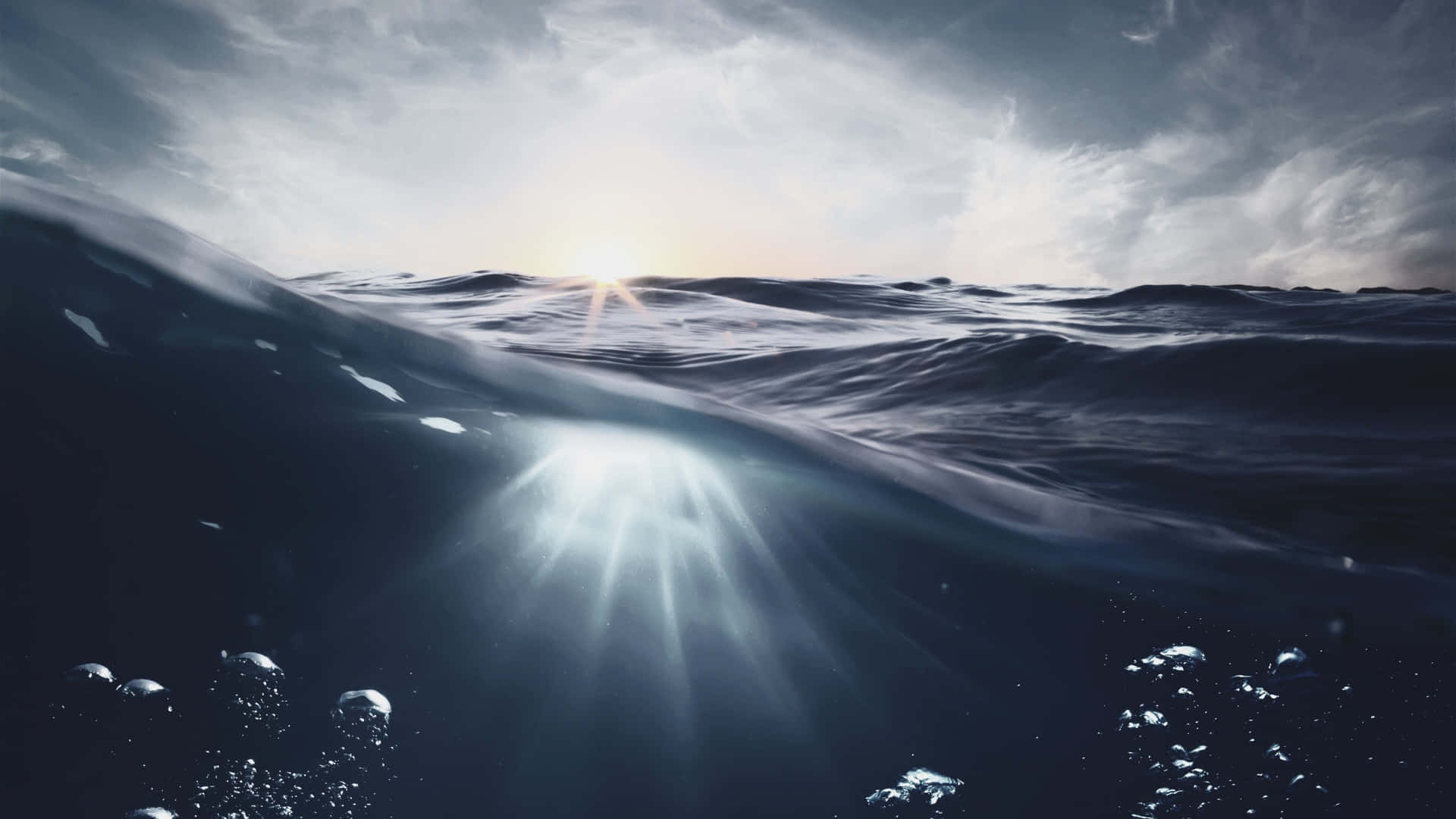  壁紙 — 陽光從上方穿透洶湧的海浪，同時氣泡在黑暗的水下前景中升起。