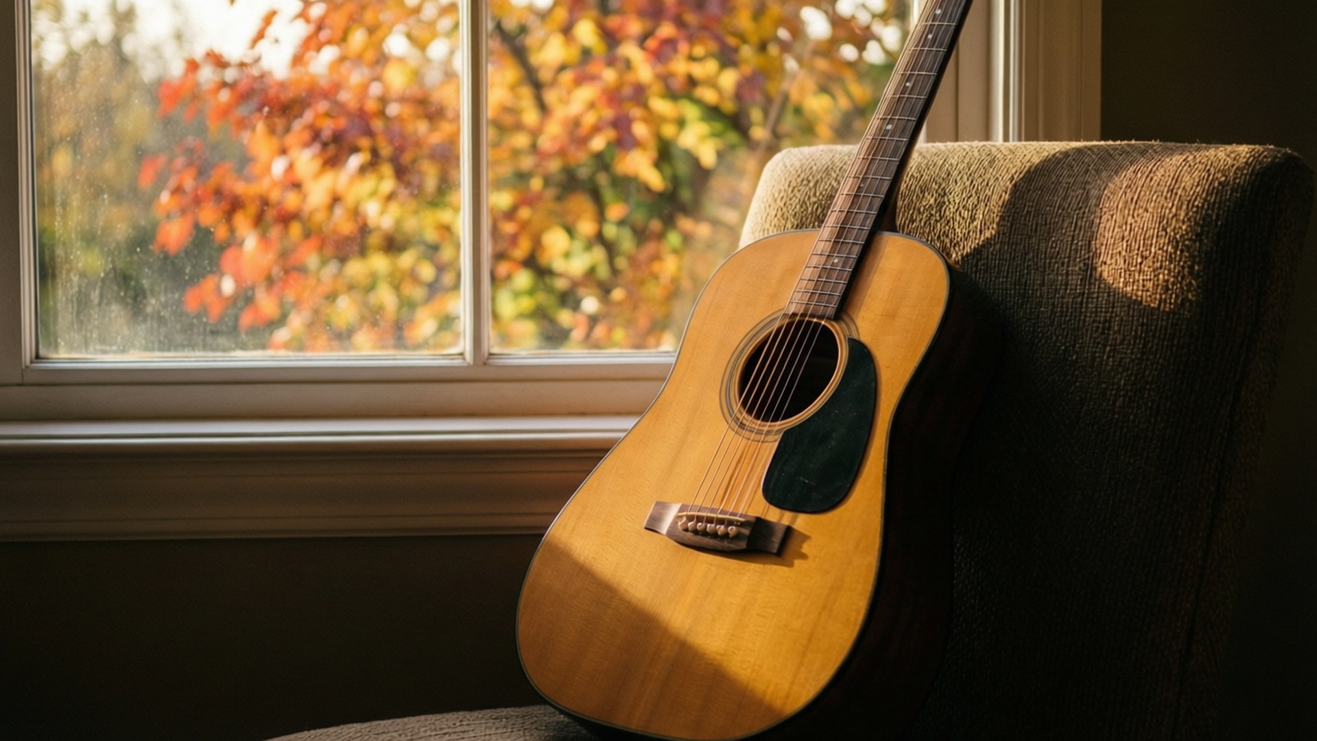 Autumn Guitar 壁紙 — 陽光照射下的原聲吉他放在一張有紋理的椅子上，旁邊的窗戶展現出充滿活力的秋葉。