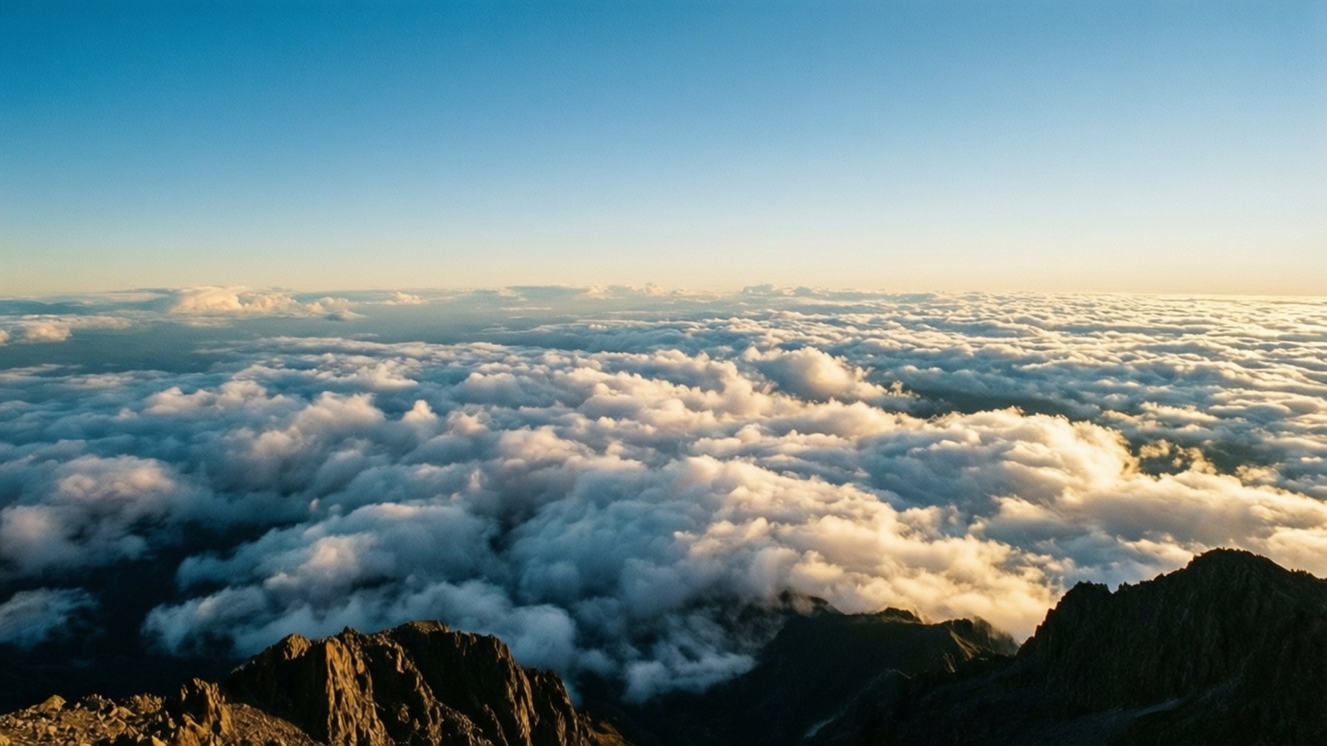 Mountain Top Clouds 壁紙 — 從山頂觀看的陽光普照的雲景，有鋸齒狀的山脊和晴朗的藍天。