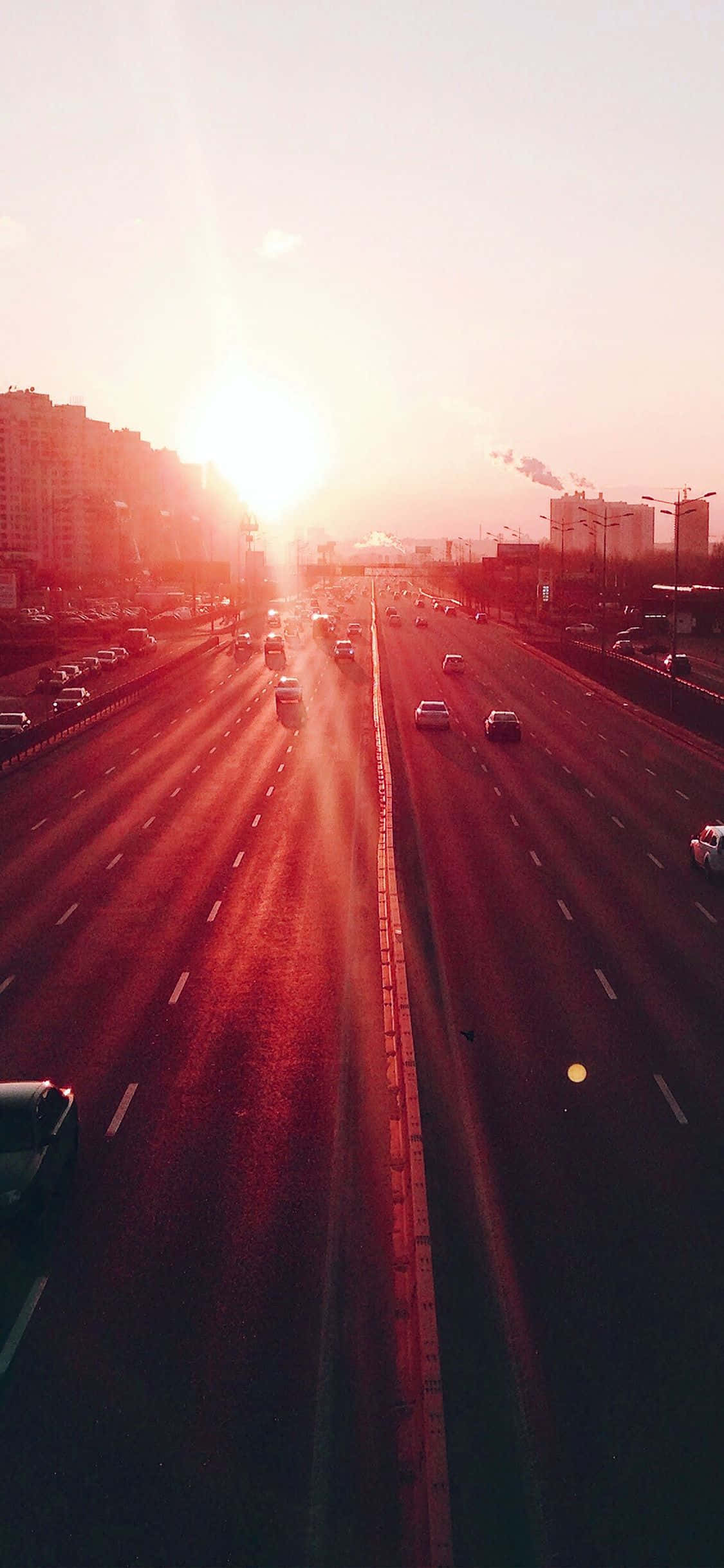 Sunset Drive 桌布 壁紙 — 夕陽以溫暖的紅光照亮多車道高速公路，汽車在都市擴展區中行駛。