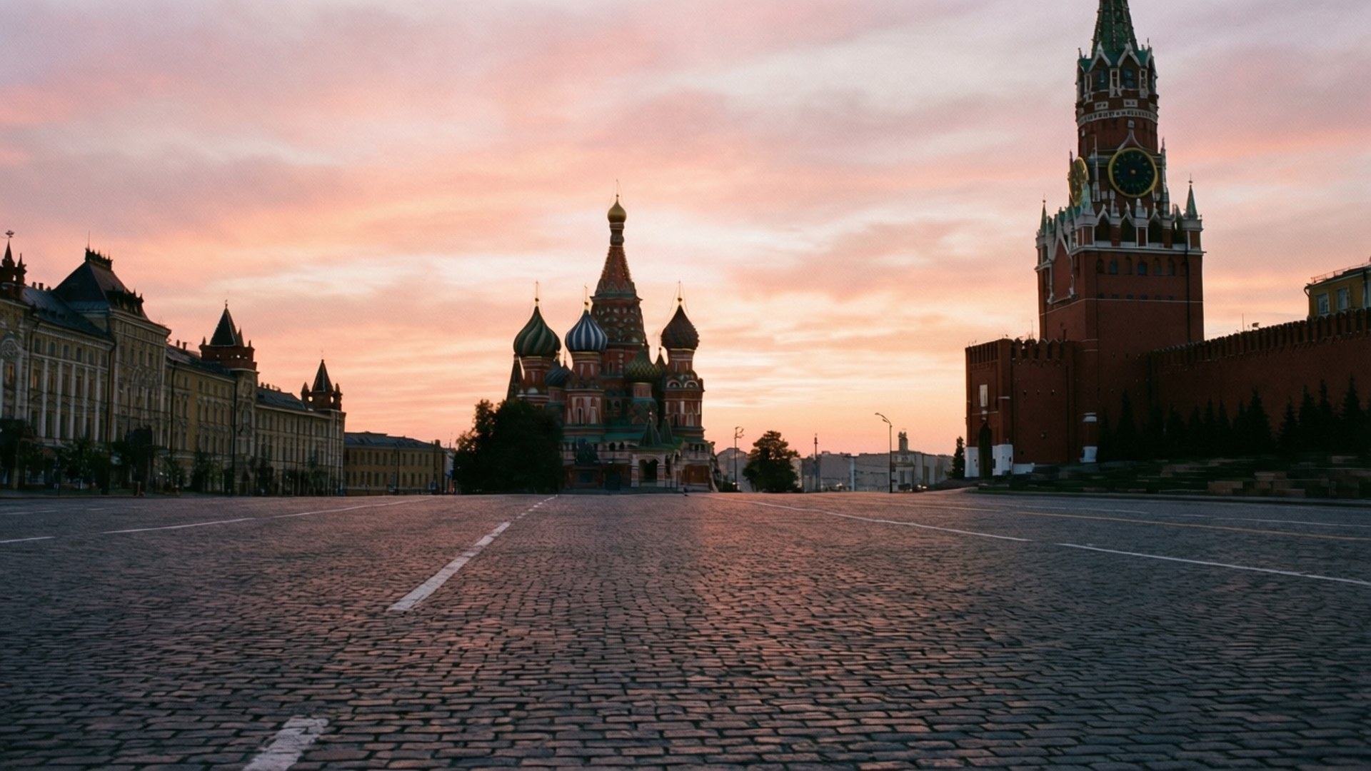 Dawn at Red Square 壁紙 — 夕陽將紅磚克里姆林宮城牆和聖瓦西里大教堂沐浴在溫暖的粉金色光芒中，灑在空無一人的鵝卵石廣場上。