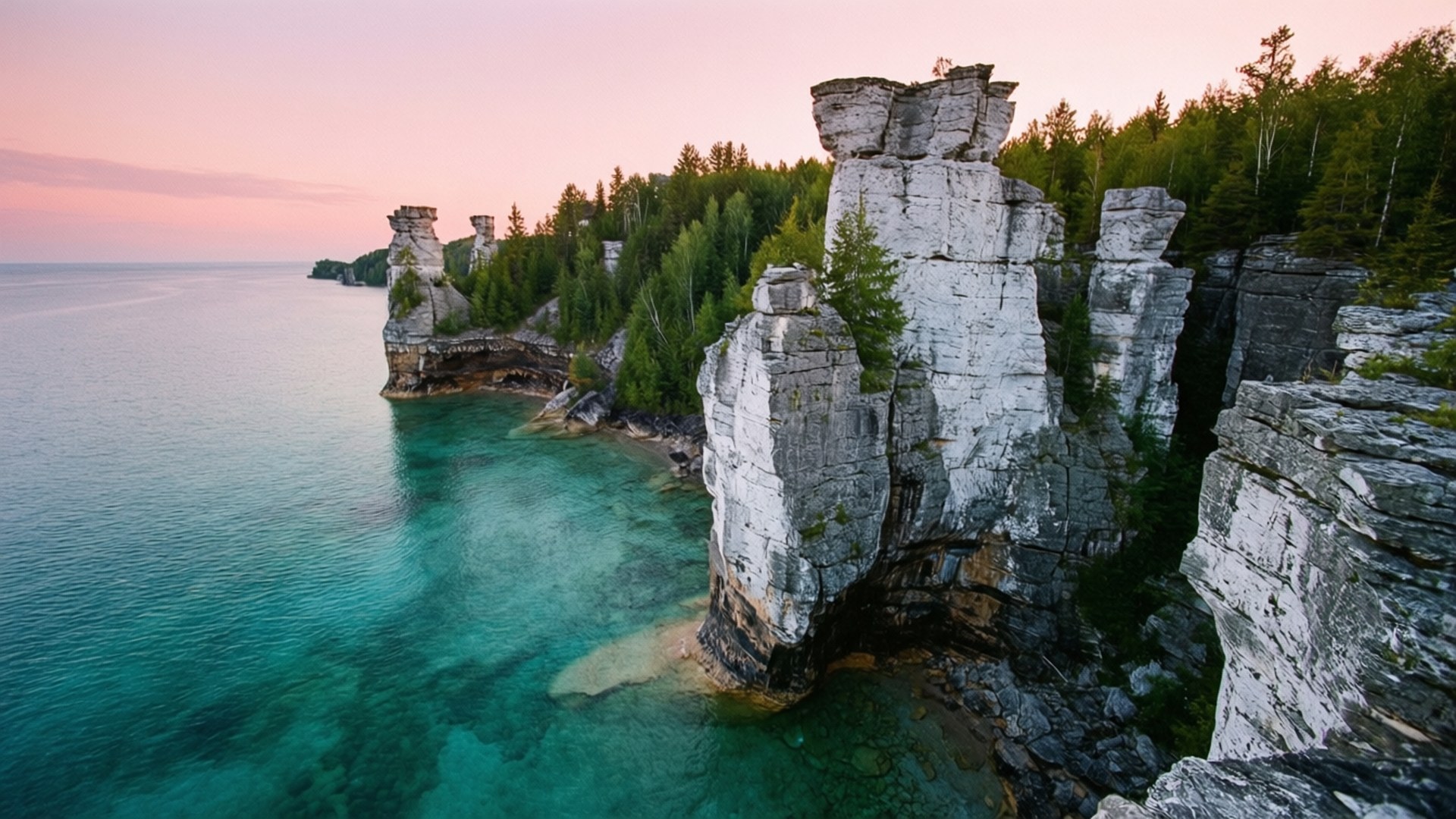Bruce Peninsula Dawn 壁紙 — 夕陽將高聳的石灰岩海蝕柱沐浴在粉紅色的光芒中，而碧綠的海水拍打著它們樹木繁茂的基部。