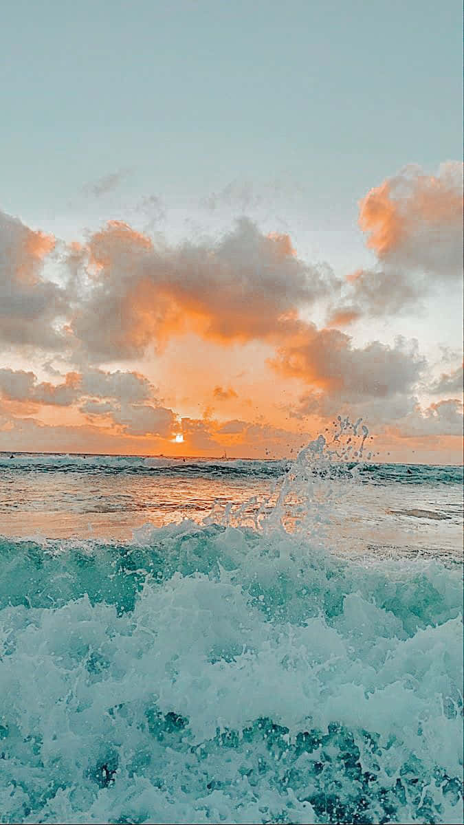  壁紙 — 夕陽將雲彩染成橙色，海浪拍打岸邊激起藍綠色泡沫。