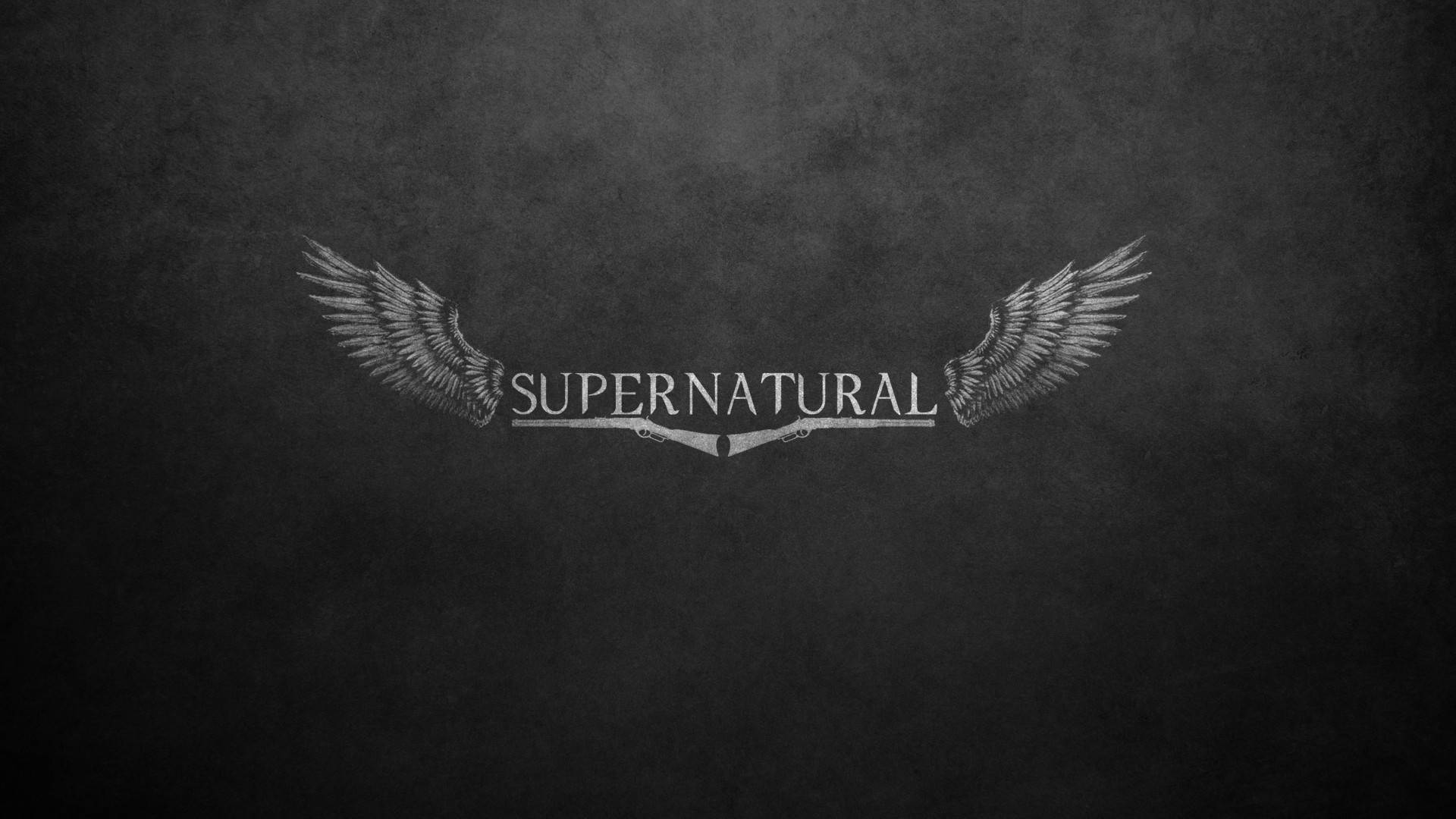 超自然 桌布 壁紙 — 「supernatural」這個字被精細的翅膀圍繞在有紋理的深灰色背景上。