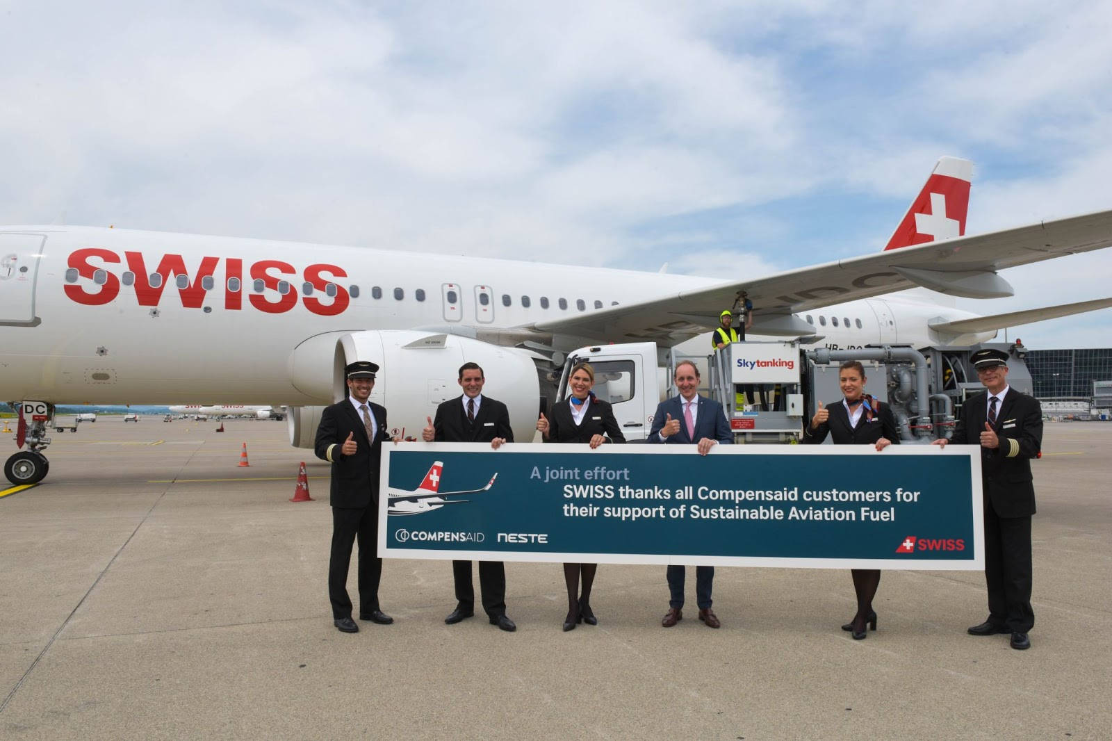 Airport 桌布 壁紙 — SWISS 航空機組人員及管理層在機場停機坪舉起橫幅，感謝 Compensaid 客戶支持永續航空燃料。
