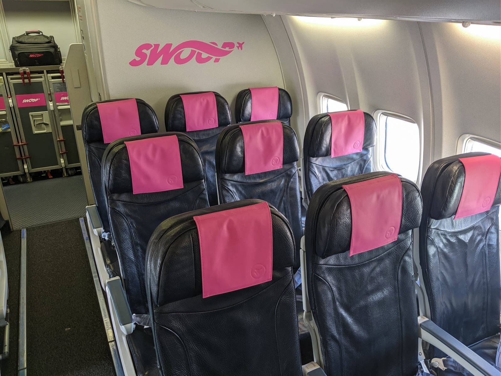 seat 桌布 壁紙 — SWOOP 飛機機艙內一排排黑色皮革飛機座椅，配有亮粉紅色頭枕套。