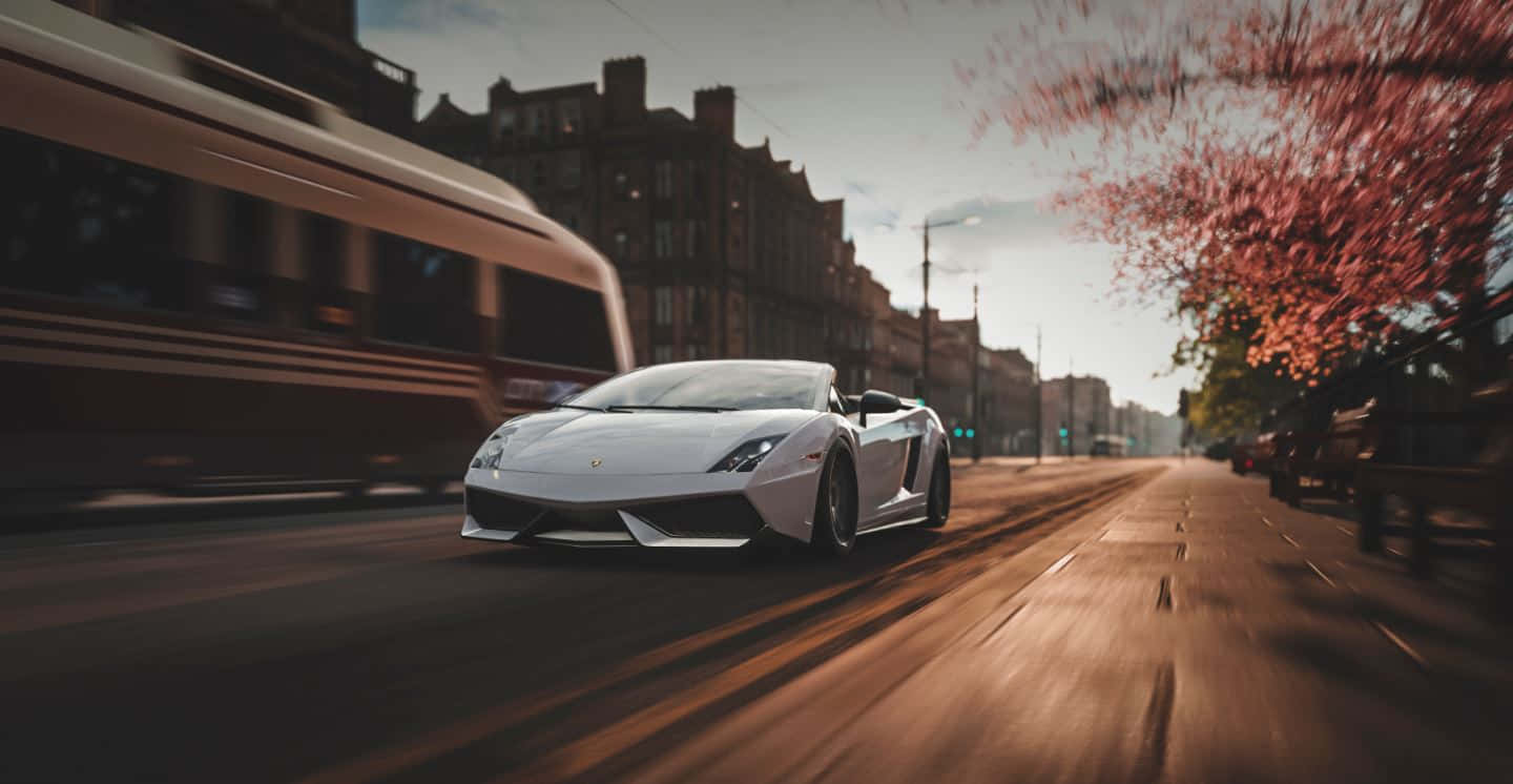 Lamborghini Gallardo 桌布 壁紙 — 一台流線型白色藍寶堅尼Gallardo Spyder在日落時分，伴隨著櫻花和移動中模糊的電車，在城市的街道上奔馳。
