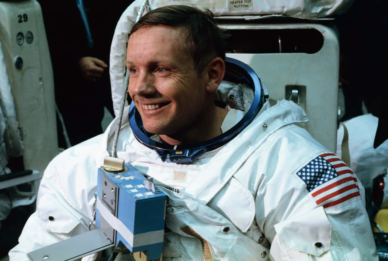 Neil Armstrong 桌布 壁紙 — 太空人尼爾·阿姆斯壯在太空船艙內穿著白色太空衣，帶有美國國旗臂章，露出溫暖的笑容。