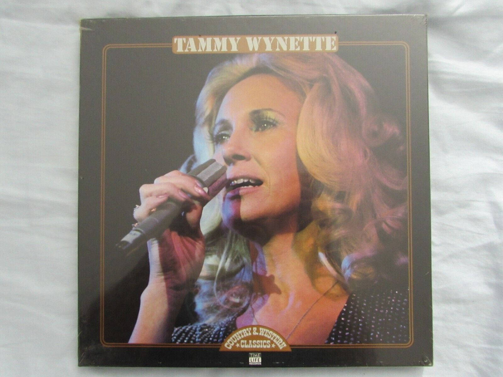 artist 桌布 壁紙 — Tammy Wynette 在一個復古鄉村音樂專輯封面上，用溫暖的燈光和柔軟的捲髮對著麥克風唱歌。