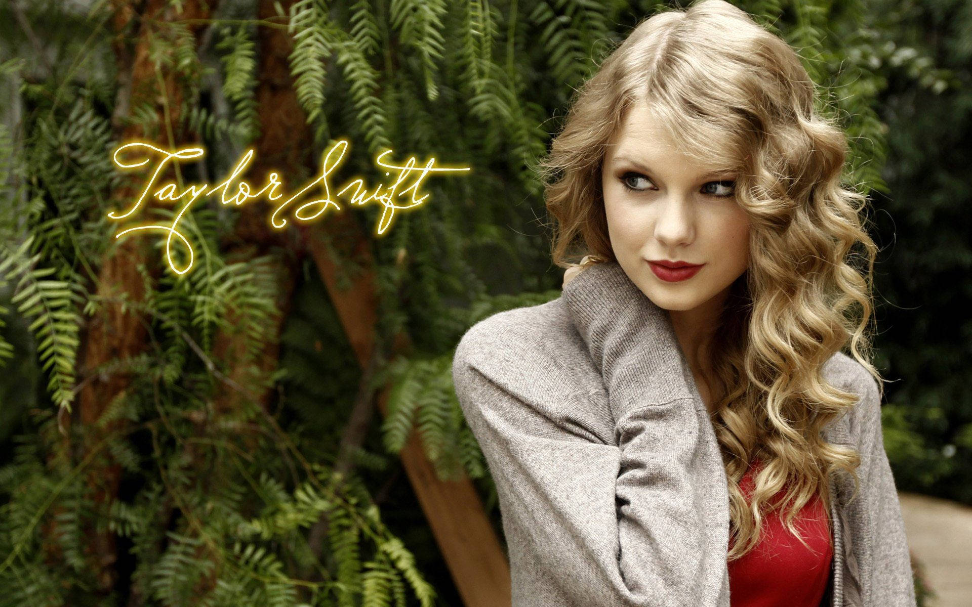 Taylor Swift 桌布 壁紙 — Taylor Swift 以捲曲金髮和紅唇在茂密綠色蕨類背景前擺姿勢，帶有發光黃色文字。