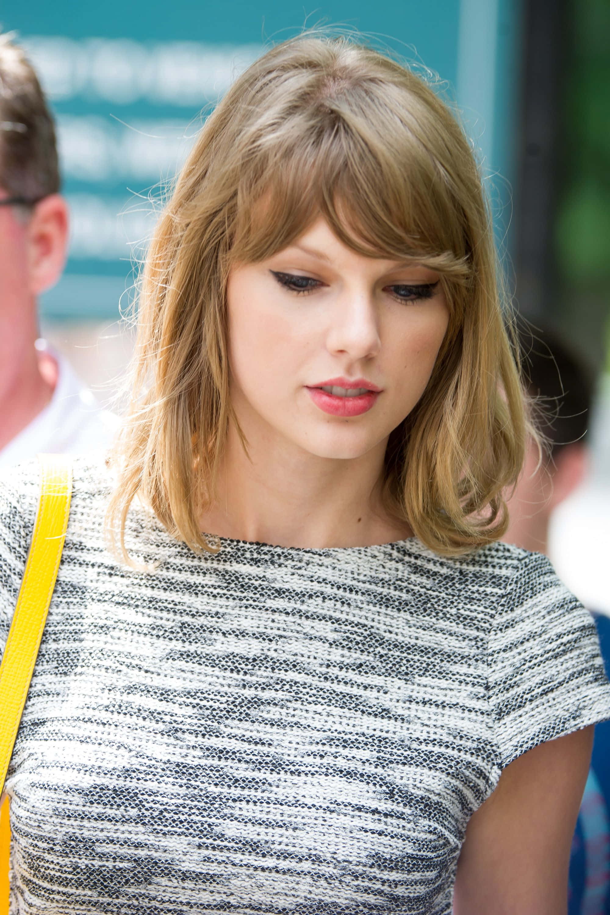 泰勒絲 桌布 壁紙 — Taylor Swift 低頭沉思，身穿質感灰白上衣，搭配黃色肩帶手袋。