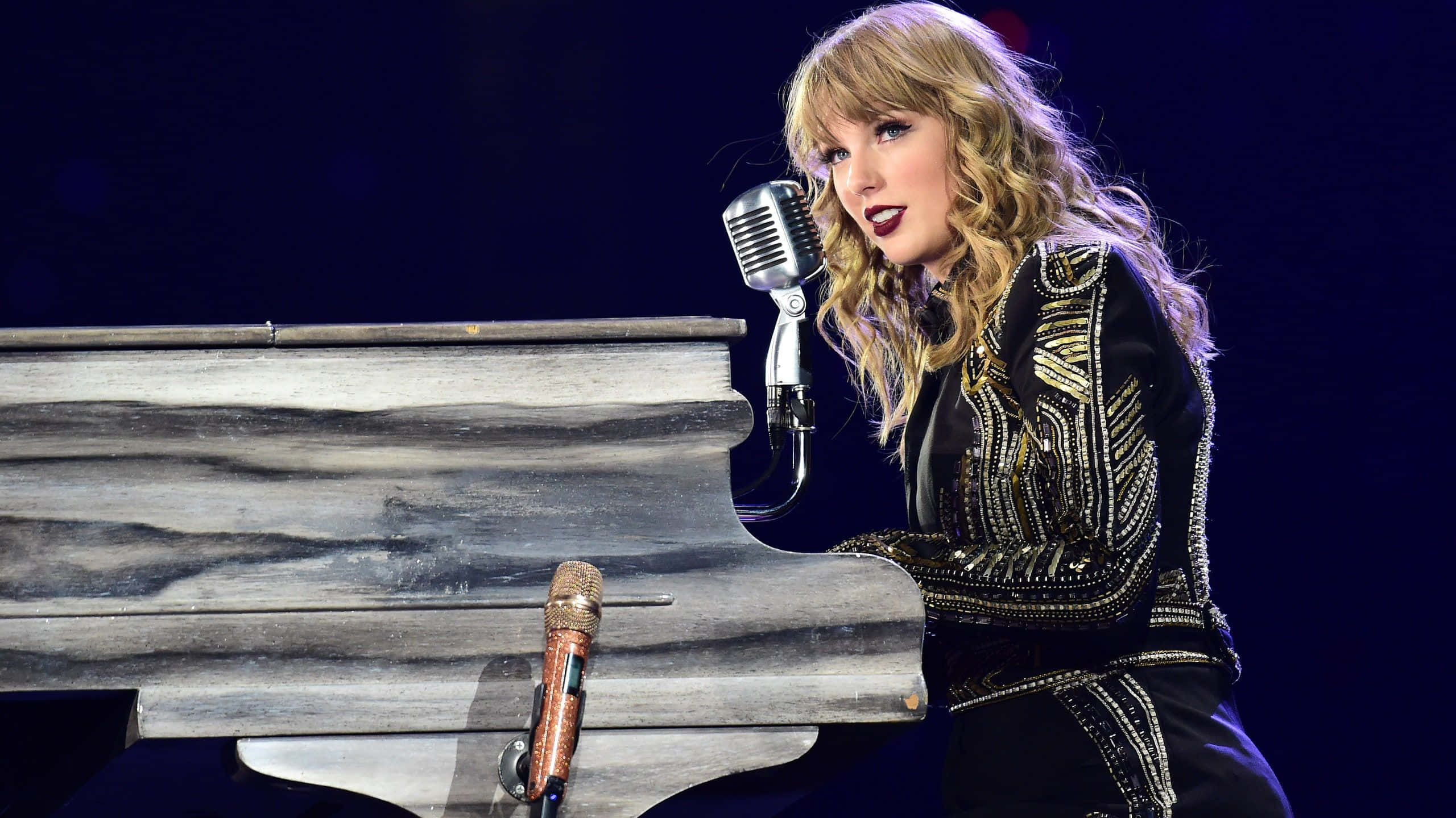 泰勒絲 桌布 壁紙 — Taylor Swift 在舞台燈光下，用復古麥克風在鋼琴前熱情演出。