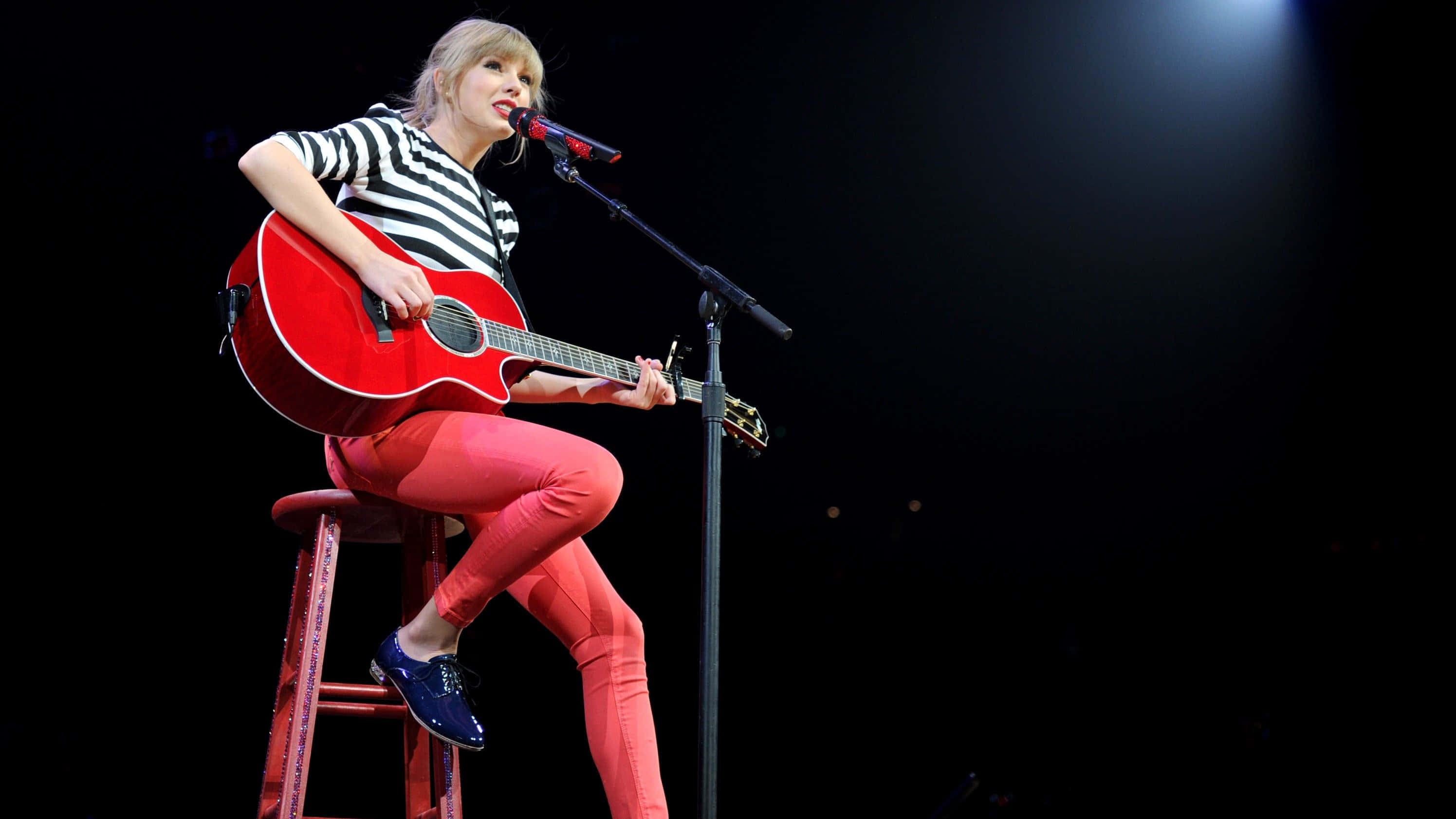 Taylor Swift Laptop 桌布 壁紙 — Taylor Swift 在舞台上坐在紅色凳子上，在聚光燈下拿著紅色木吉他表演。