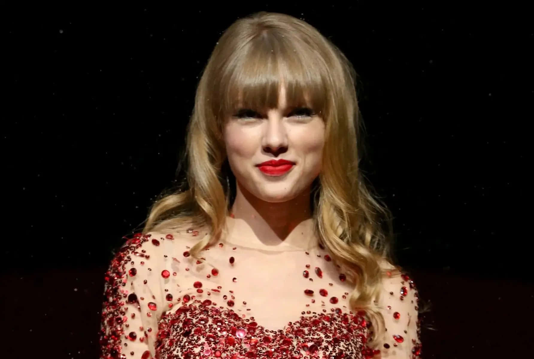 泰勒絲 桌布 壁紙 — Taylor Swift 穿著閃亮的紅色亮片連衣裙，在黑暗的星空背景下微笑。