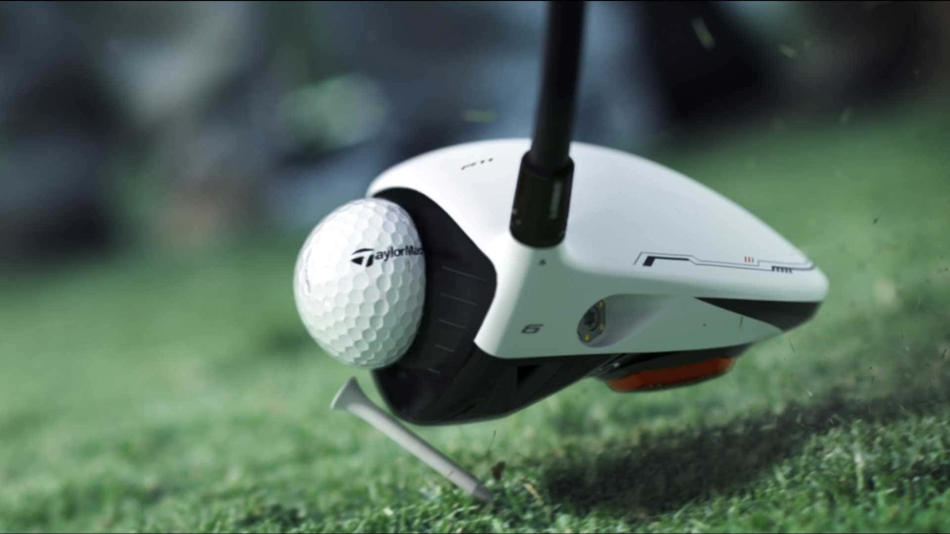 Awesome Golf 桌布 壁紙 — TaylorMade 高爾夫球桿在茂密的綠色發球台上擊打白色高爾夫球，草葉飛揚。