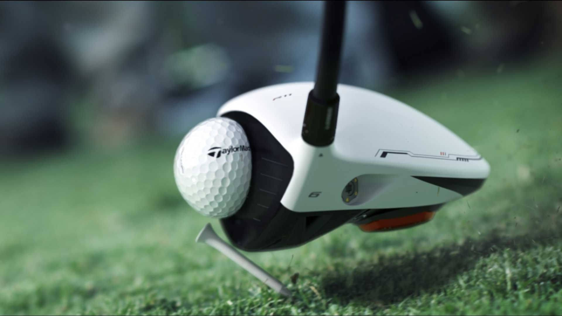高爾夫 桌布 壁紙 — TaylorMade 高爾夫球桿頭擊中綠色發球檯上的白色高爾夫球，草葉以慢動作飛散。