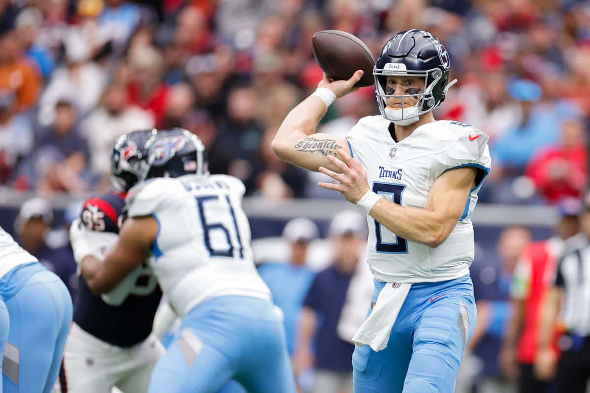  壁紙 — 一位身穿白色和淺藍色球衣的田納西泰坦四分衛在NFL日間比賽中擲出橄欖球，背景是模糊的體育場人群。