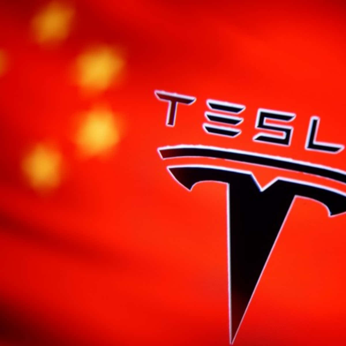 特斯拉 桌布 壁紙 — Tesla 標誌清晰對焦在帶有金色星星的模糊紅色中國國旗上。