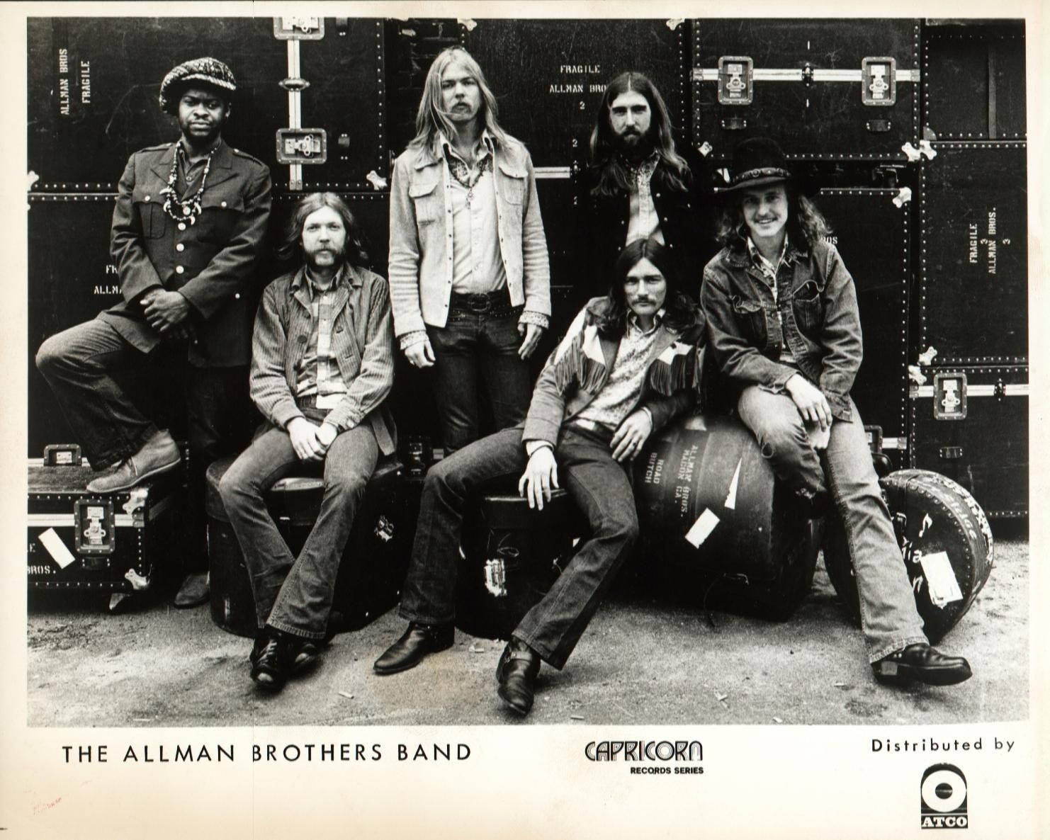 音樂 桌布 壁紙 — The Allman Brothers Band 自信地穿著復古牛仔褲和靴子，以堆疊的設備箱和鼓為背景擺姿勢。